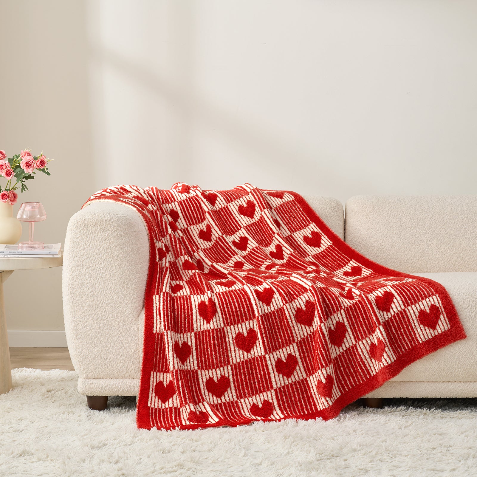 Red heart-patterned blanket draped over a beige sofa in a living room. #color_Red/Cream