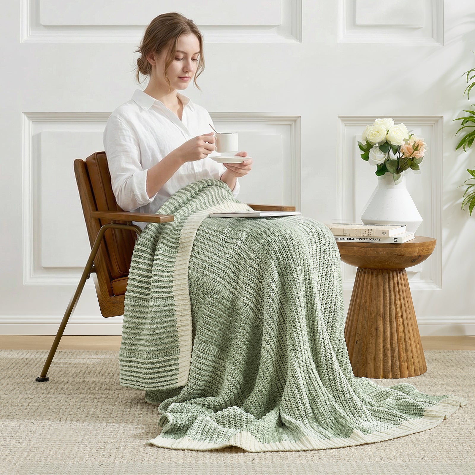 Woman sitting on a chair with a green blanket draped over her, holding a cup. #color_Two-tone Green