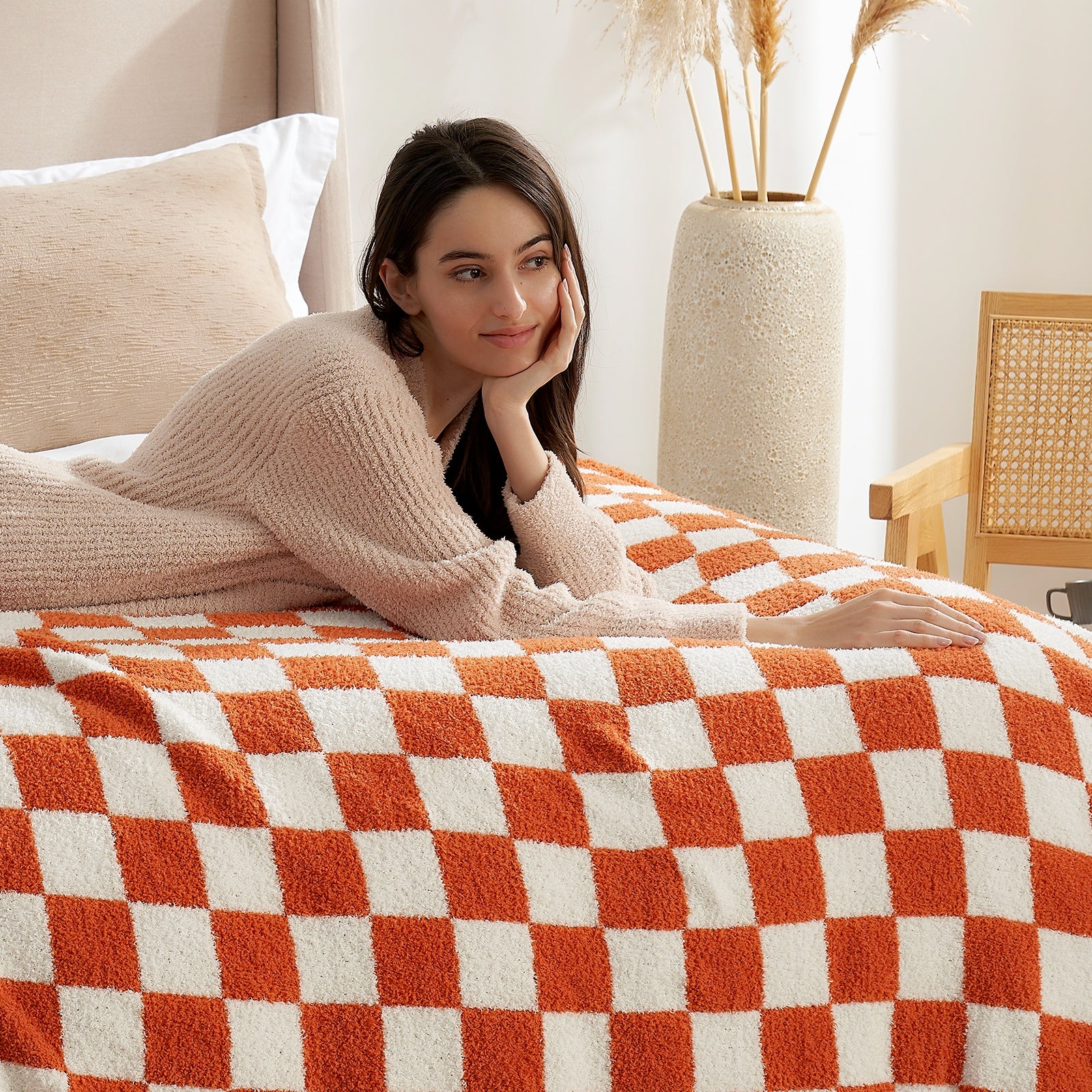 Woman lying on a bed with an orange and white checkered blanket in a cozy room. #color_Checkered Burnt Orange