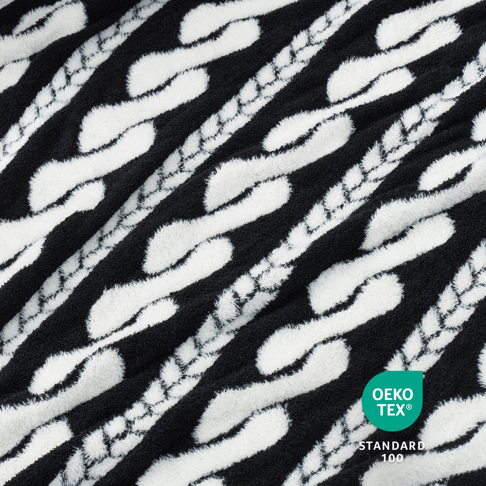 Close-up of Snuggle Sac black and white Cable pattern Faux Fur Knit Throw Blanket textured fabric with OEKO-TEX logo.#color_Black