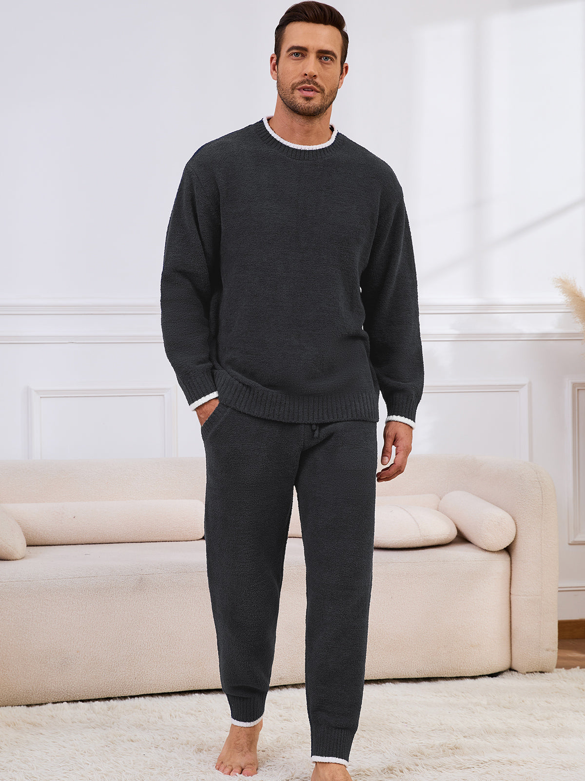 Man wearing a dark gray sweater and pants in a living room setting. #color_Dark Grey