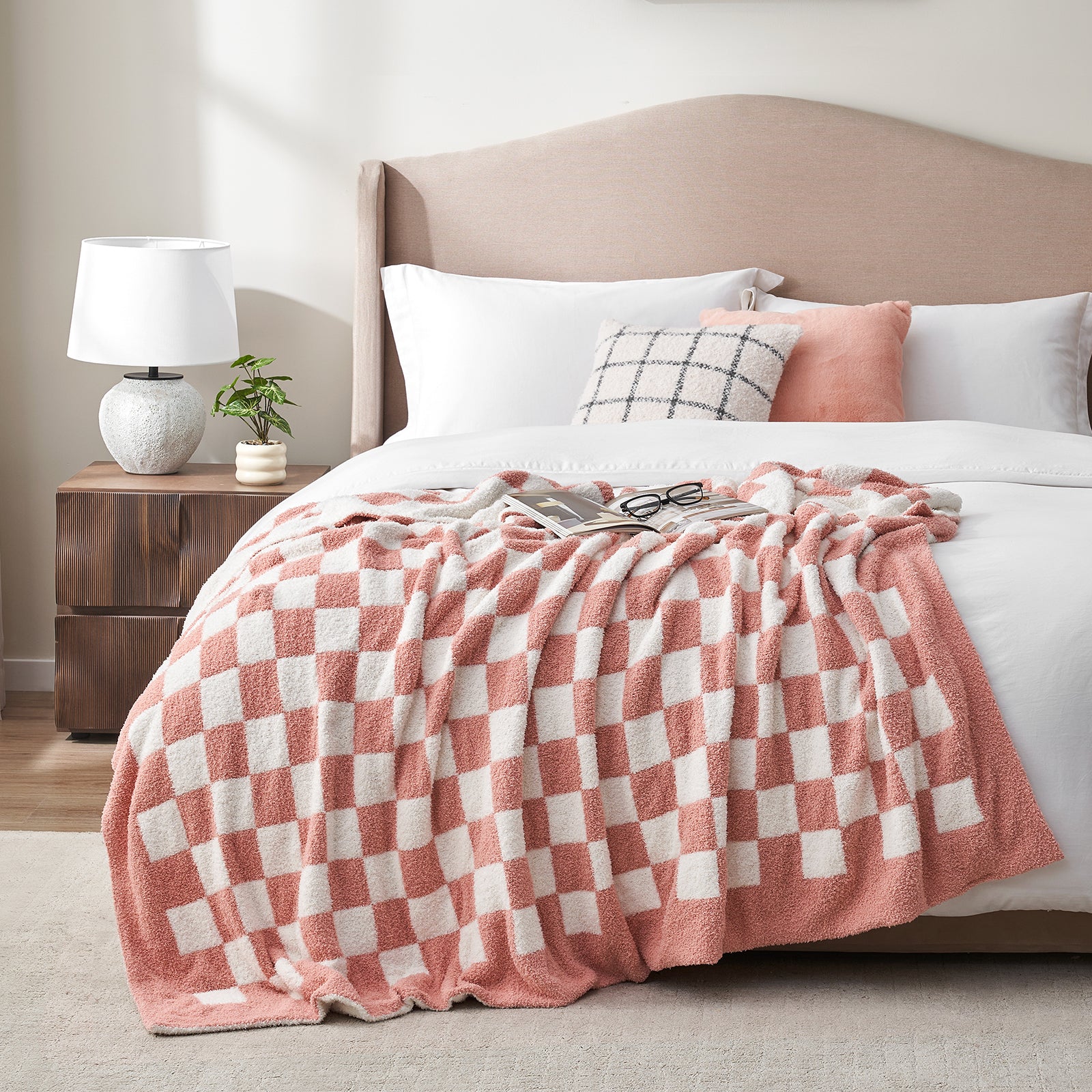 Bed with pink and white checkered blanket, pillows, and a lamp on a nightstand. #color_Checkered Pink