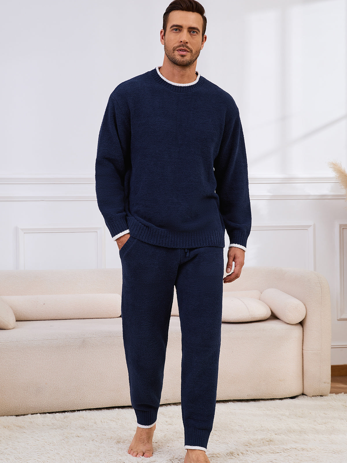 Man wearing a navy blue sweater and pants set in a living room. #color_Navy