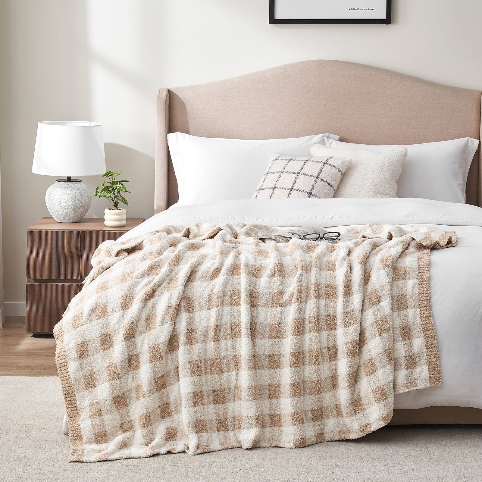 Bedroom with a bed featuring a plaid blanket, pillows, and a nightstand with a lamp. #color_Plaid Beige