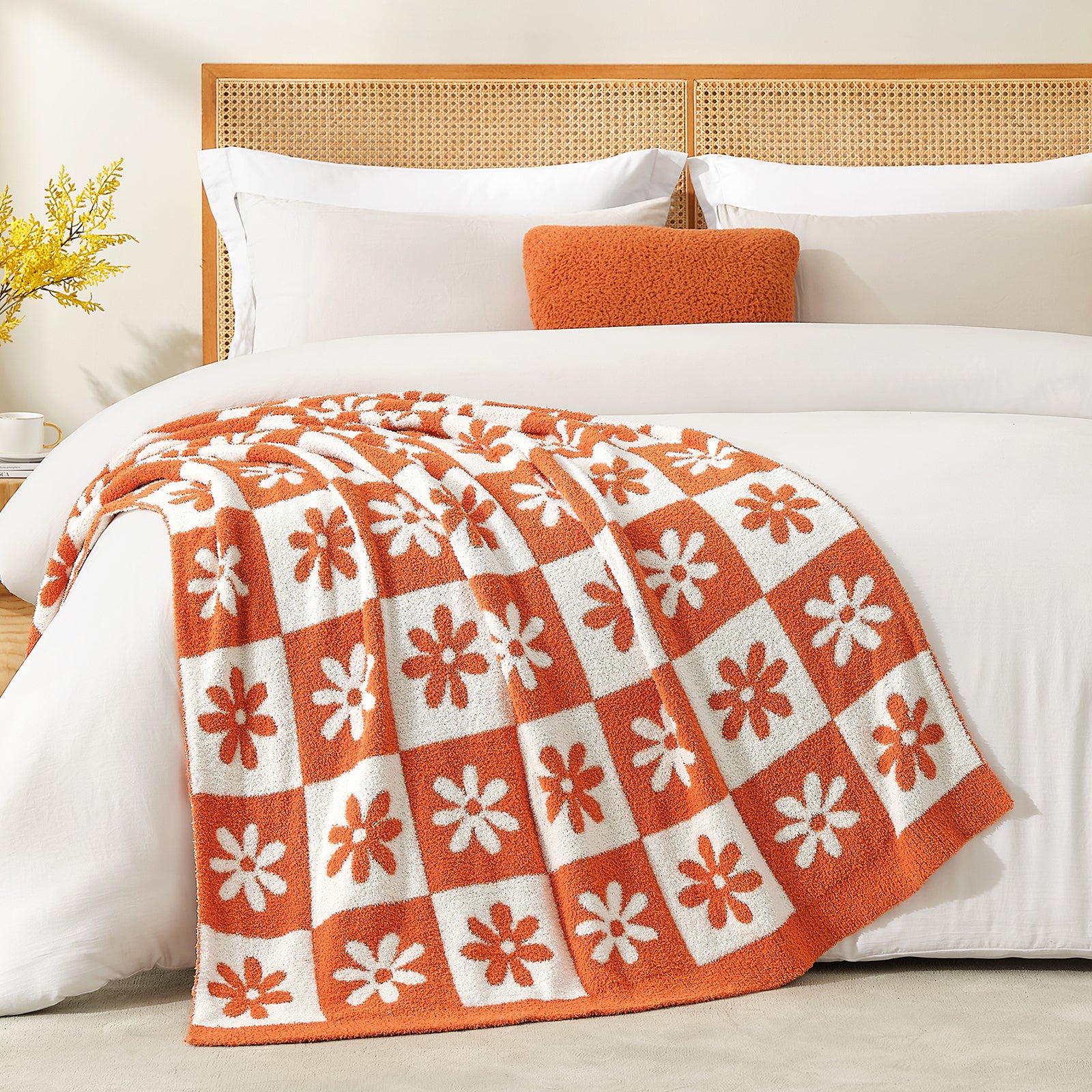 Orange and white patterned blanket on a bed with white pillows and an orange pillow. #color_Orange