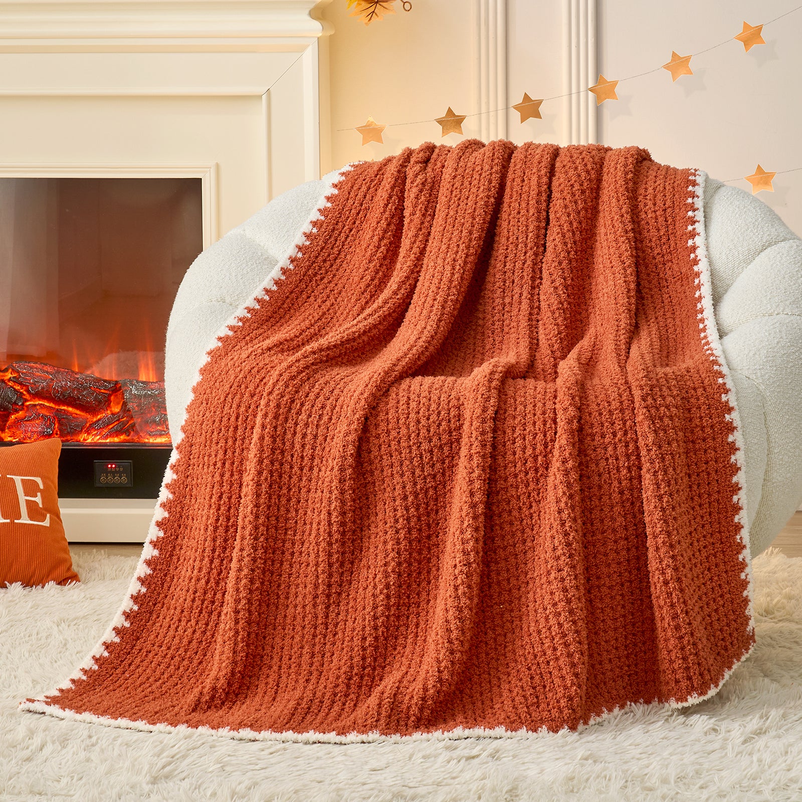 Orange knitted blanket draped over a white armchair in front of a fireplace. #color_Orange