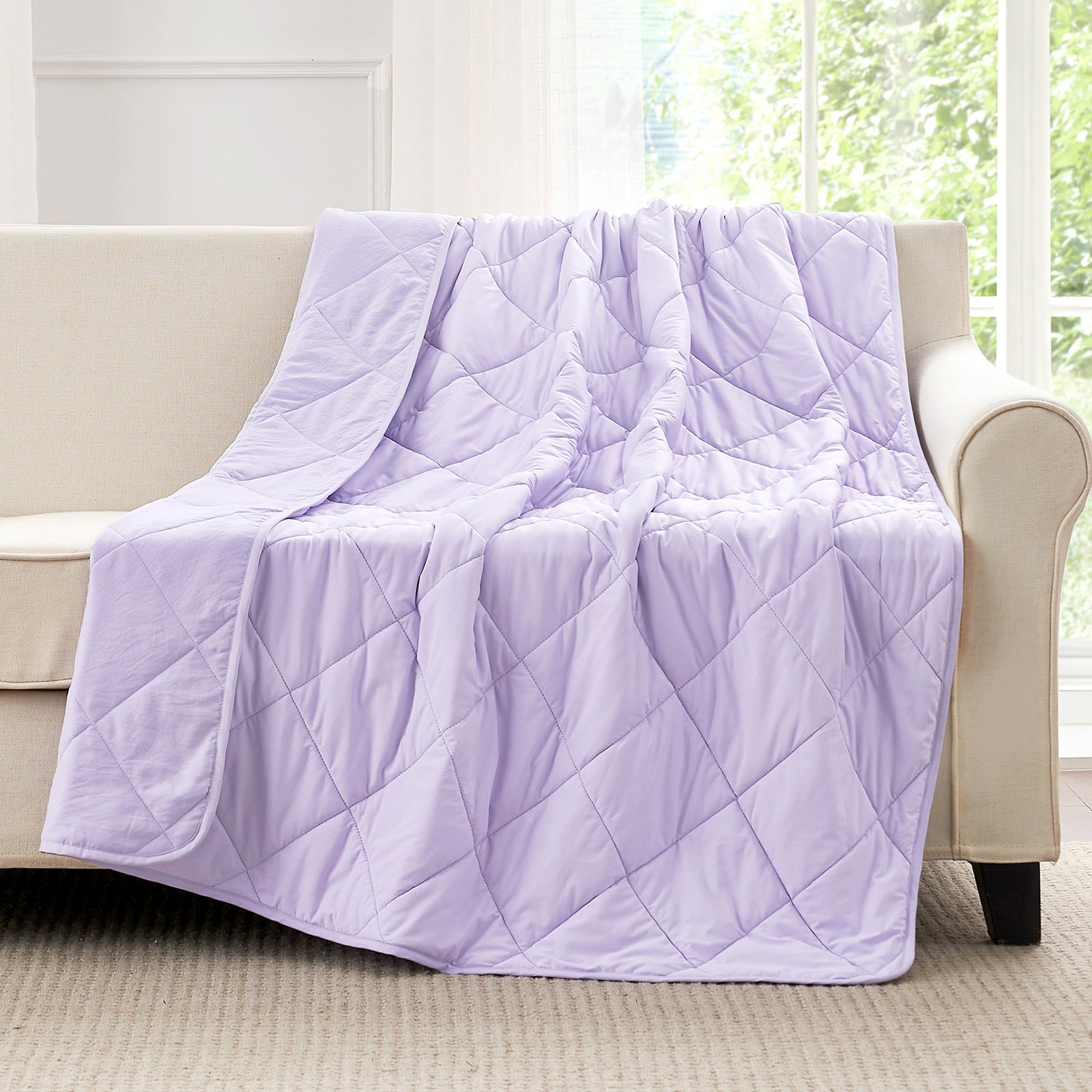 Purple cooling blanket draped over a beige sofa in a room with large windows.#color_Purple