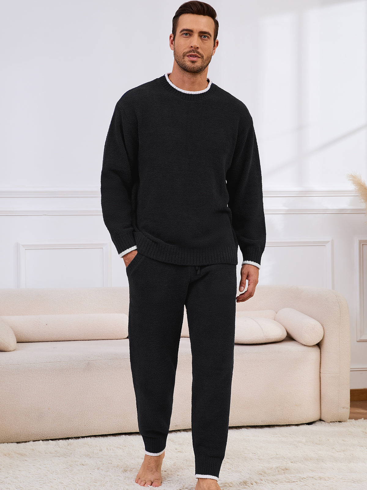 Man wearing a black sweater and pants in a living room setting. #color_Black