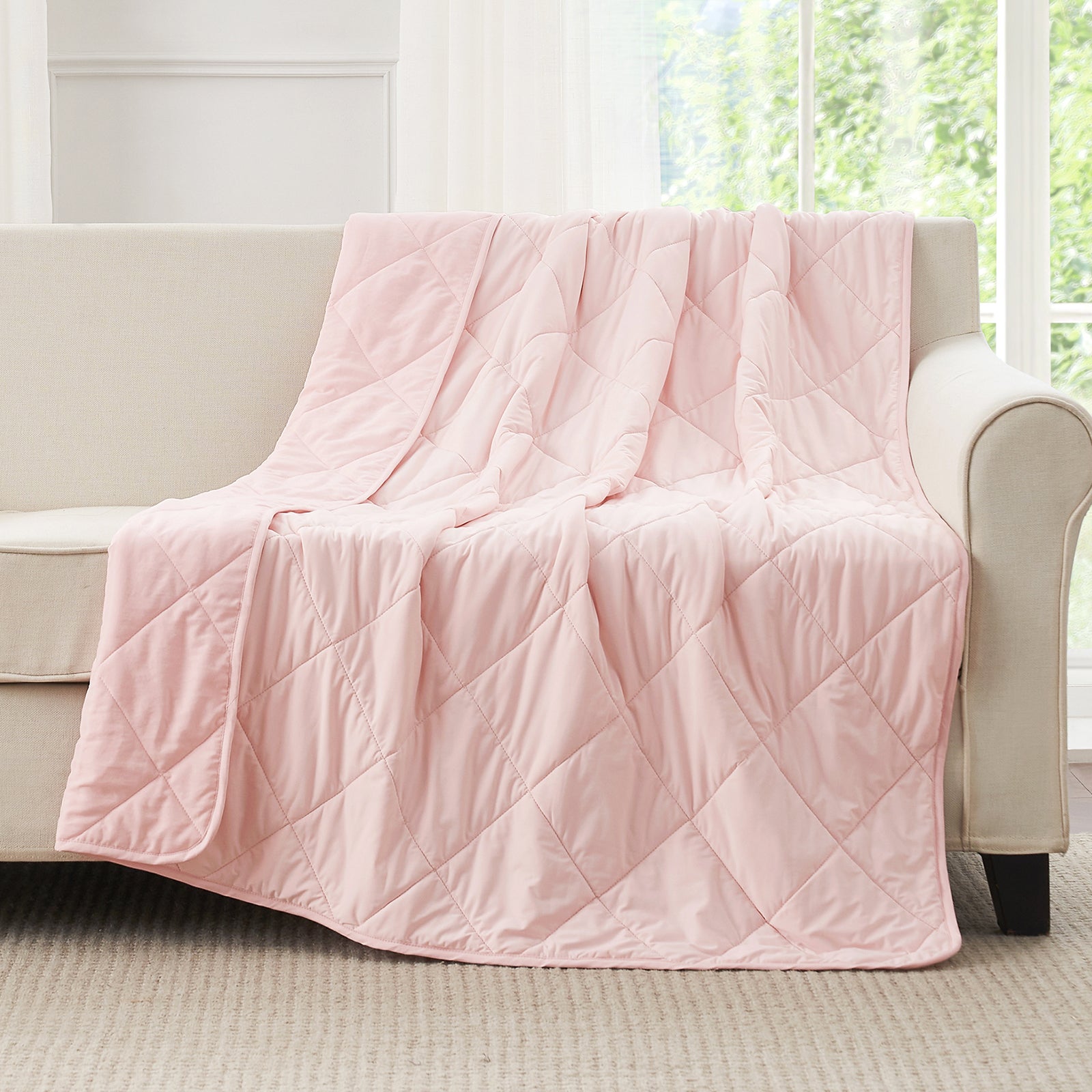 Pink cooling blanket draped over a beige sofa in a room with large windows.#color_Pink