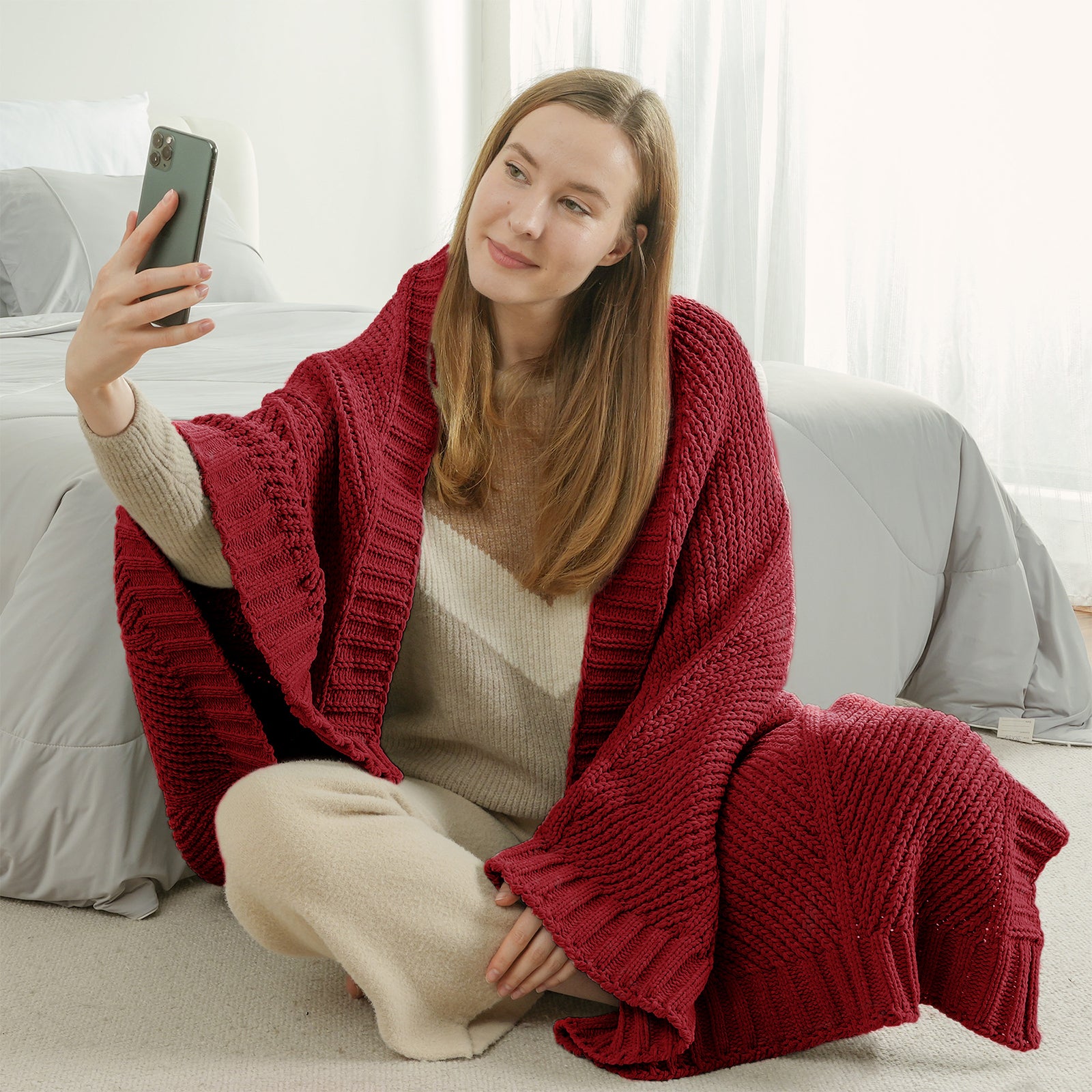 Woman sitting on the floor wrapped in a chenille knit throw blanket in Red taking a selfie #color_Red