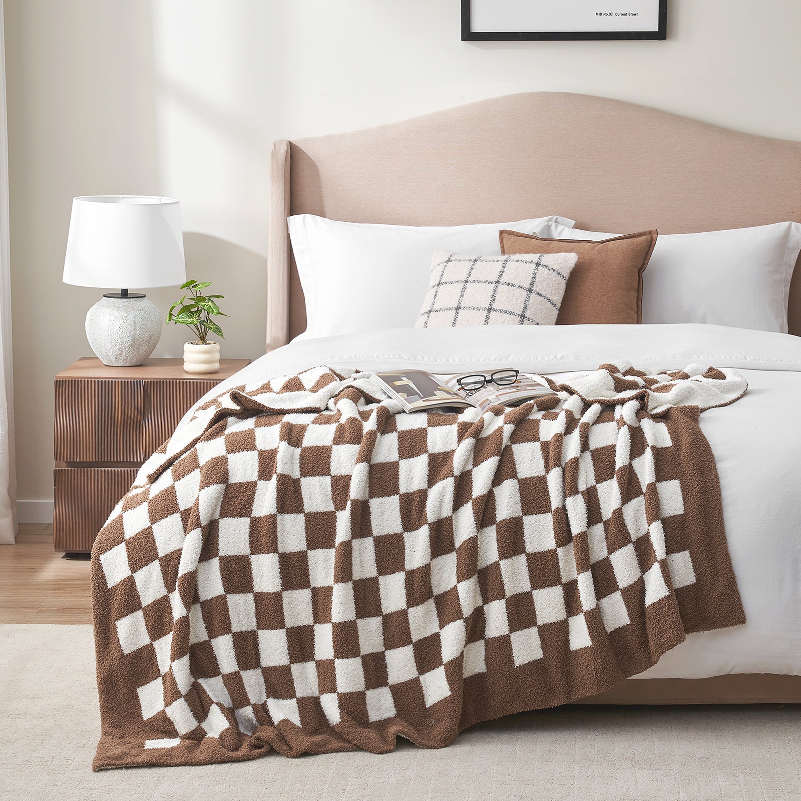 Bedroom with a bed featuring a brown and white checkered blanket, pillows, and a nightstand with a lamp. #color_Checkered Brown