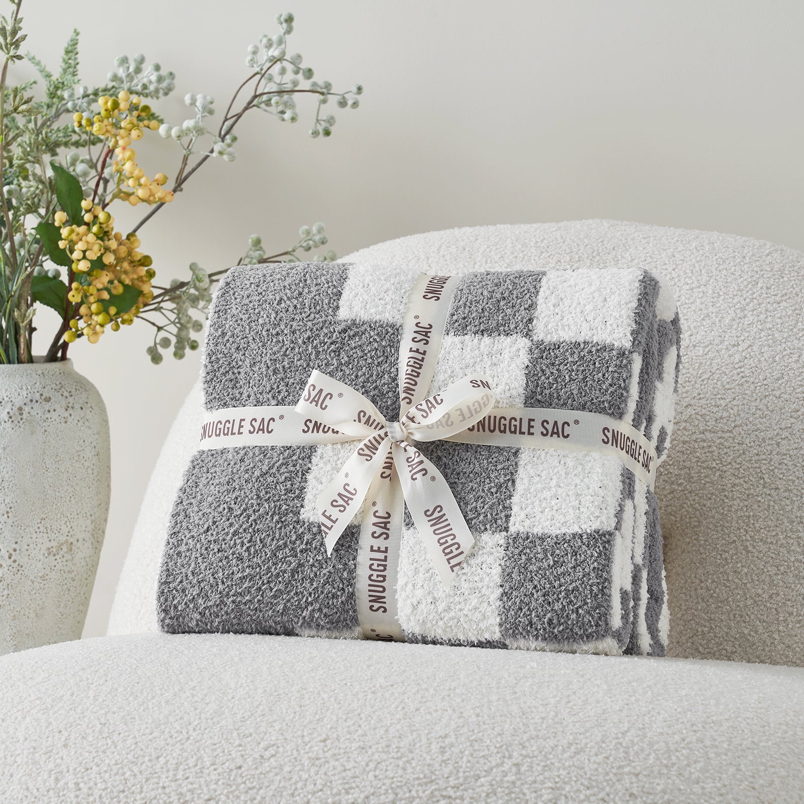 Plaid blanket with a bow on a chair next to a vase of flowers #color_Checkered Grey