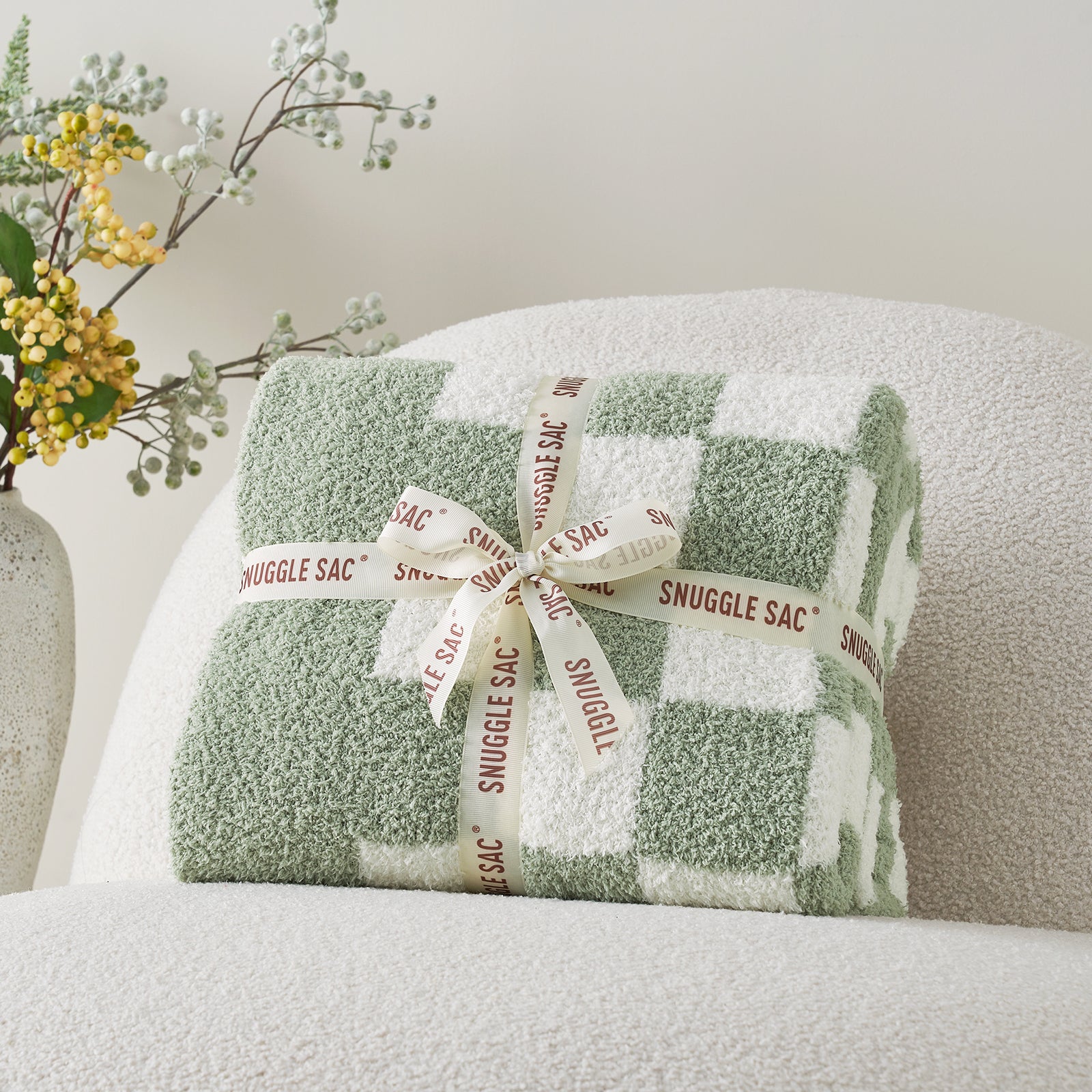 Green checkered blanket with a bow labeled 'Snuggle Sac' on a white surface. #color_Checkered Sage Green