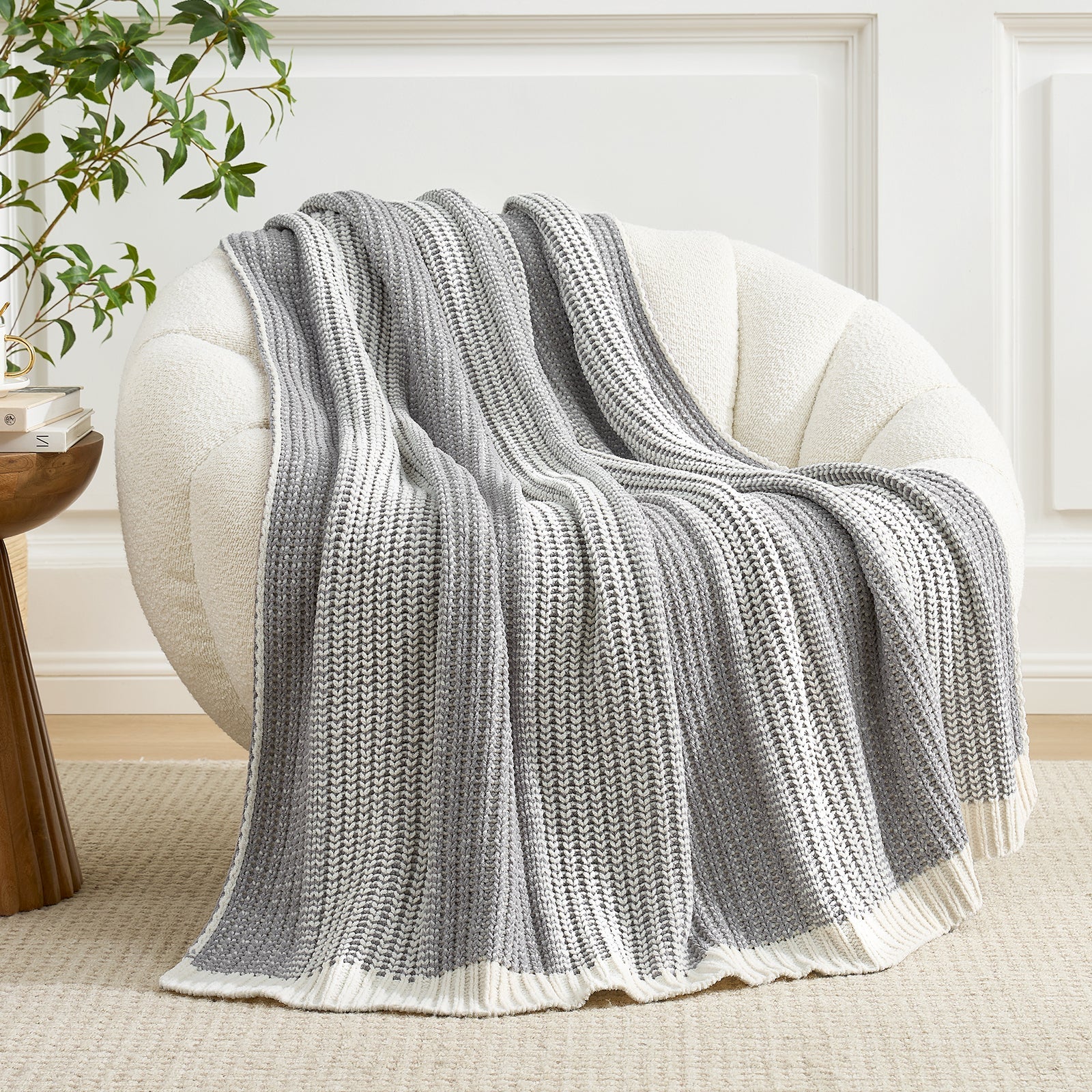 Grey and white striped blanket draped over a white armchair in a room with a plant and side table. #color_Two-tone Grey