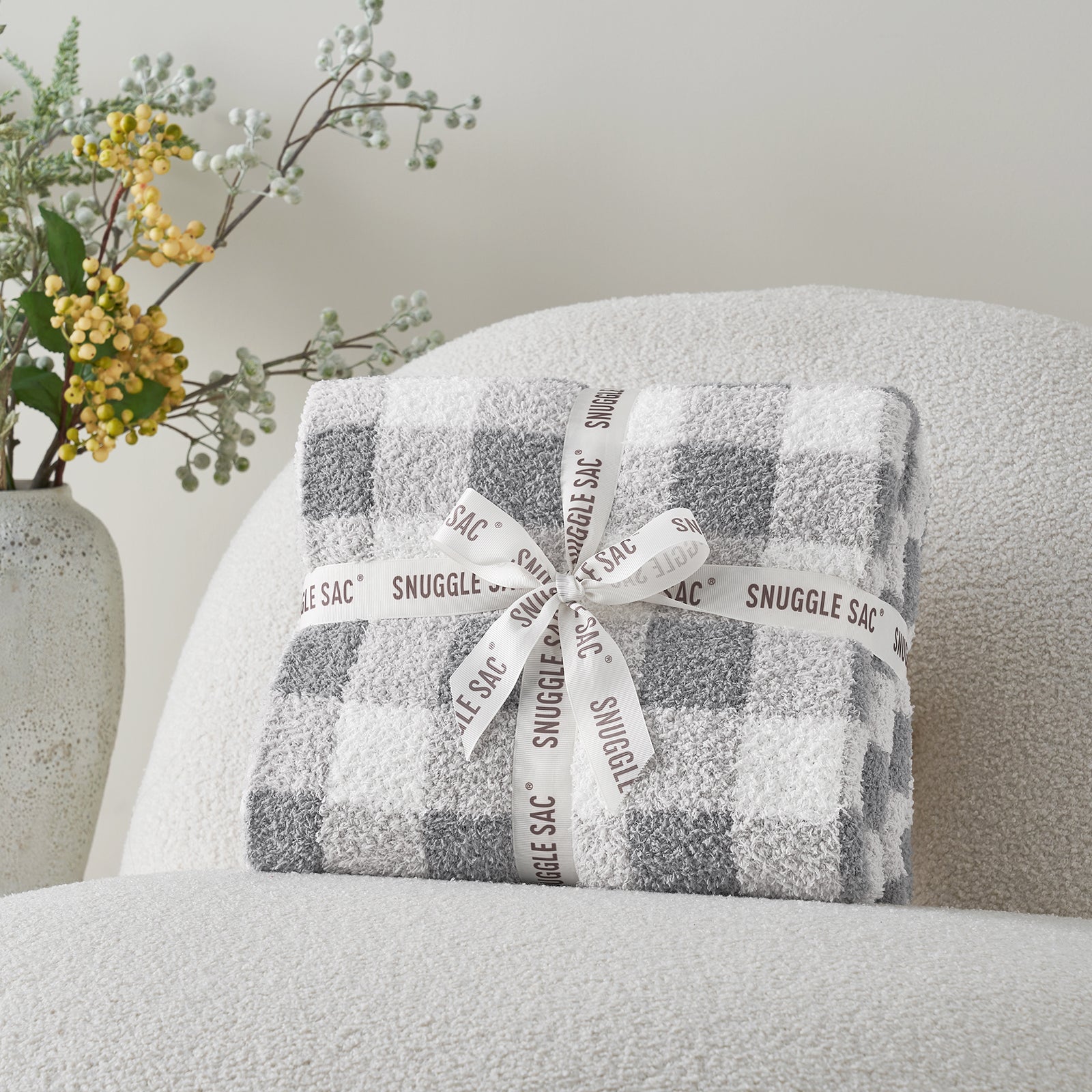 Plaid-patterned Snuggle Sac wrapped with a ribbon on a gray chair. #color_Plaid Grey
