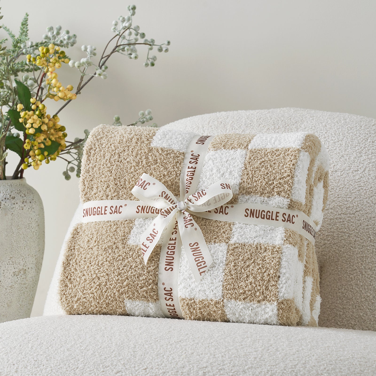 Plush blanket with a checkered pattern and 'Snuggle Sac' branding on a chair. #color_Checkered Beige