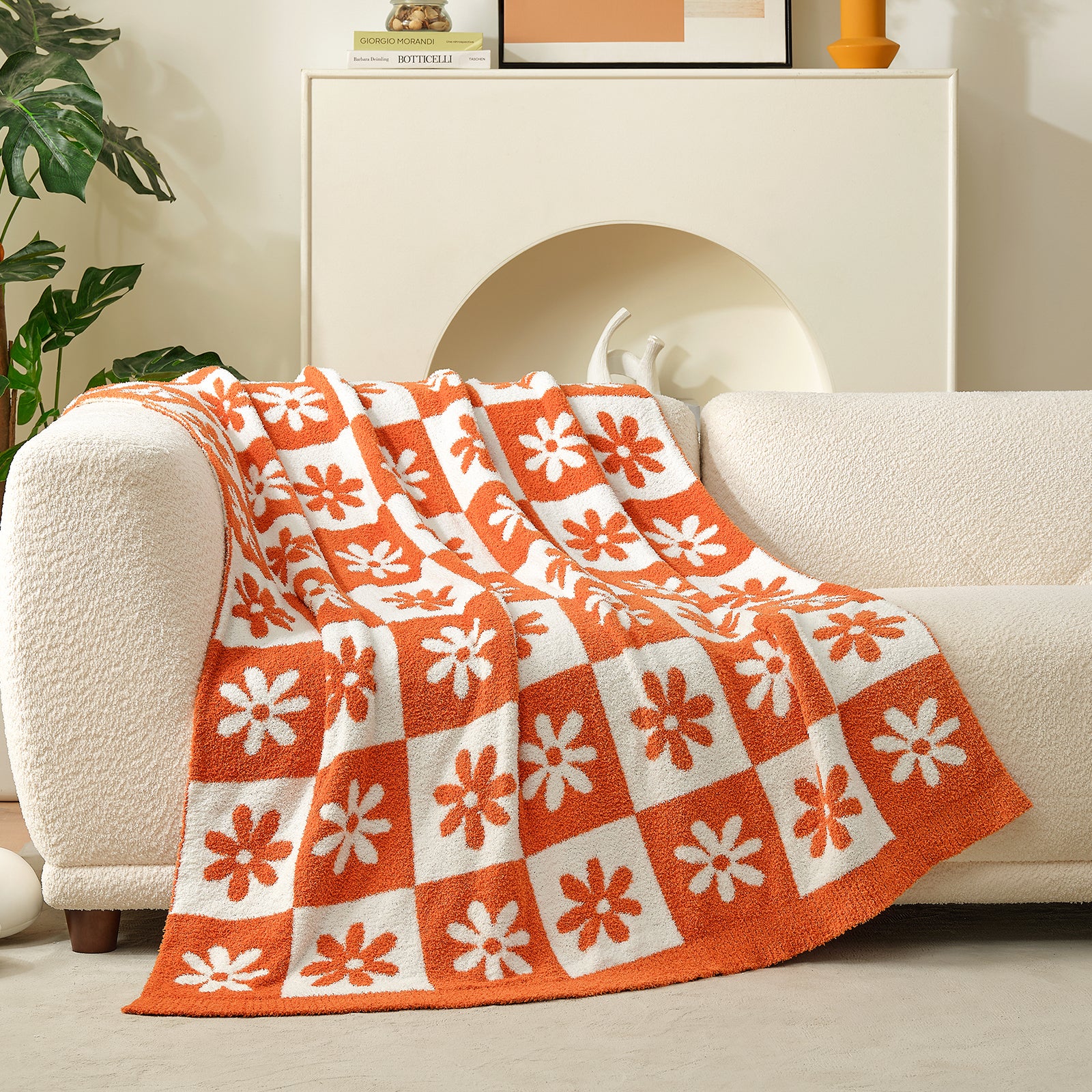 Orange and white patterned blanket draped over a white sofa in a living room setting. #color_Orange