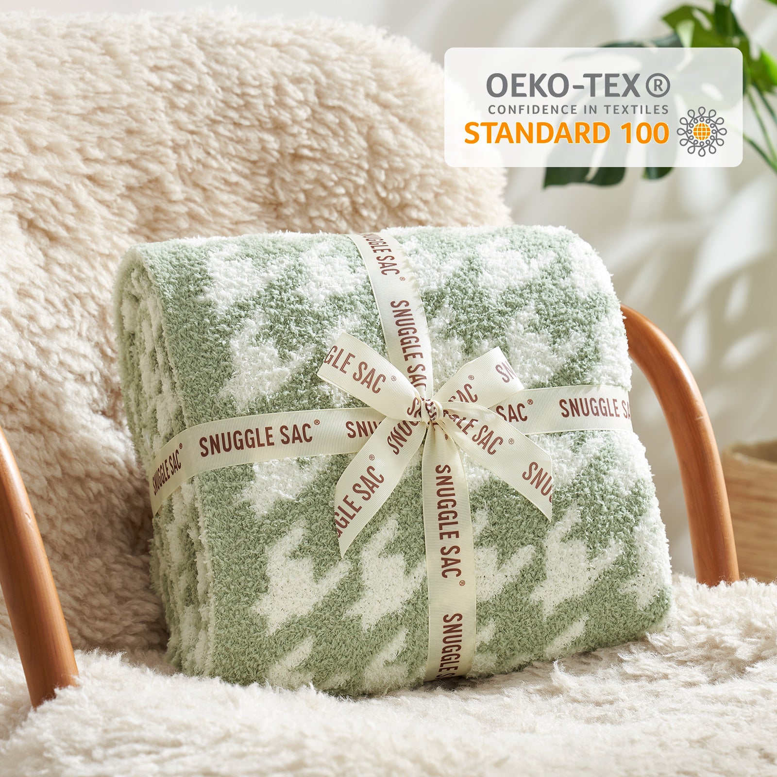 Rolled-up green blanket with 'Snuggle Sac' label on a soft surface, OEKO-TEX Standard 100 logo visible. #Color_Sage Green
