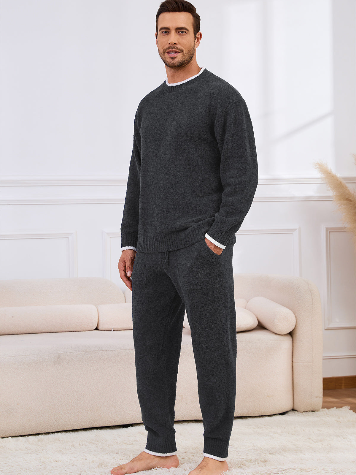 Man wearing a dark gray sweater and pants in a living room setting. #color_Dark Grey