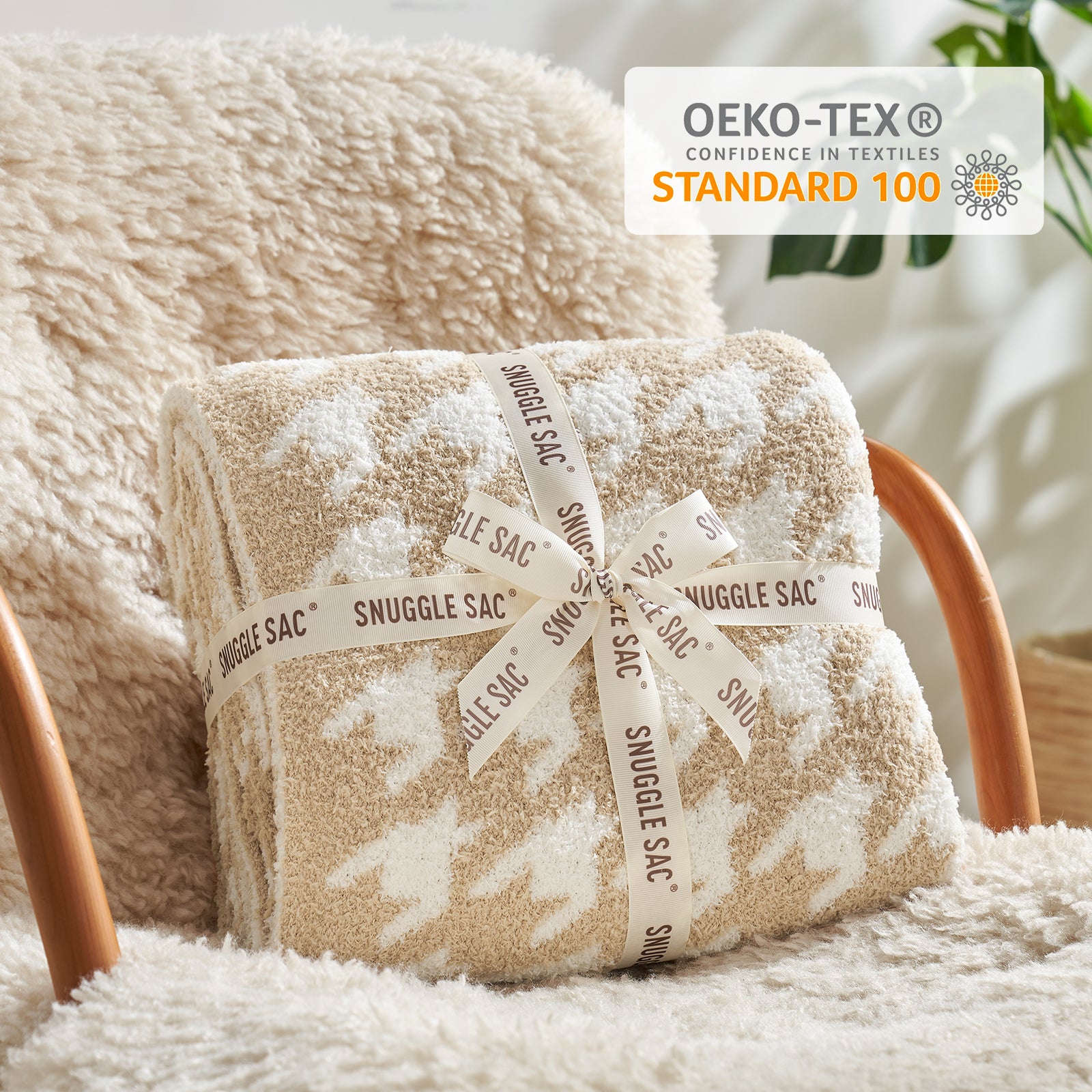 Folded beige blanket with white patterns on a chair, featuring OEKO-TEX Standard 100 logo. #color_Beige