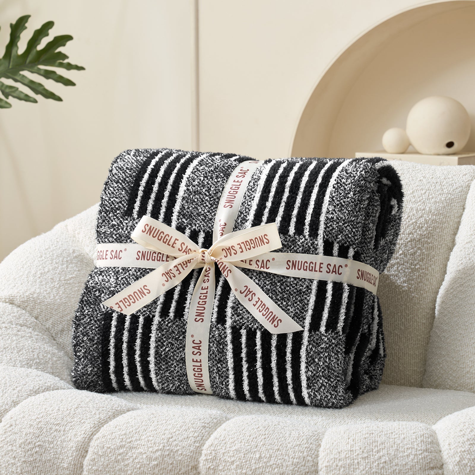 Black and white striped blanket with 'Snuggle Sac' branding on a beige couch. #color_Heather Black