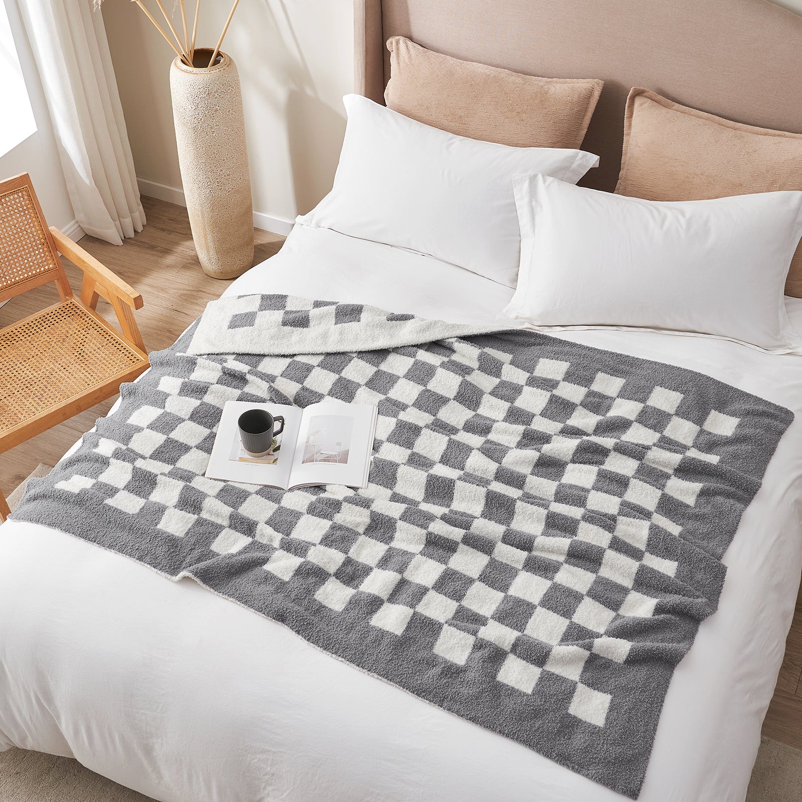 Bed with a checkered gray and white blanket, pillows, and a small table with a cup and book. #color_Checkered Grey