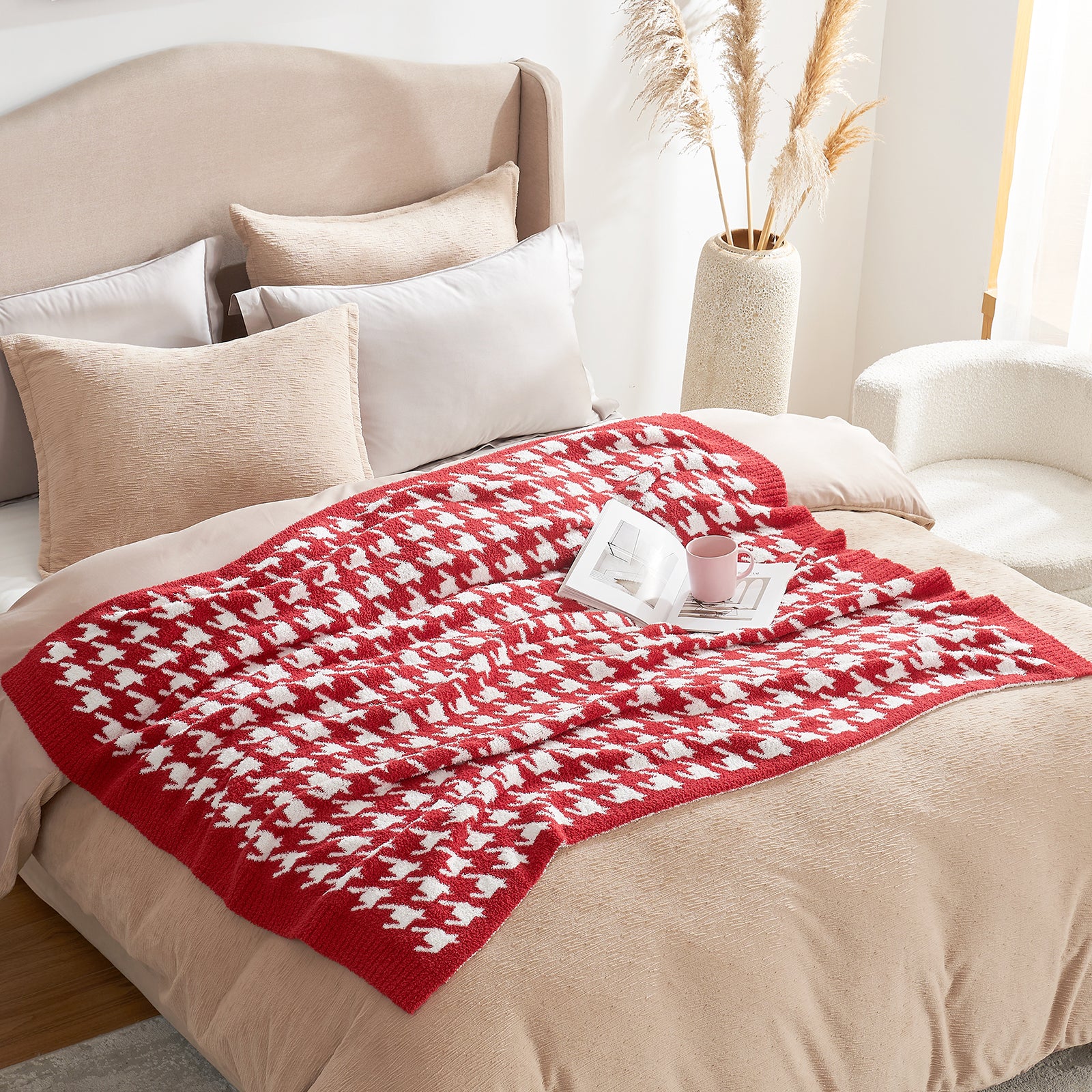 Red and white patterned blanket on a bed with pillows and a cup in a cozy room. #color_Red