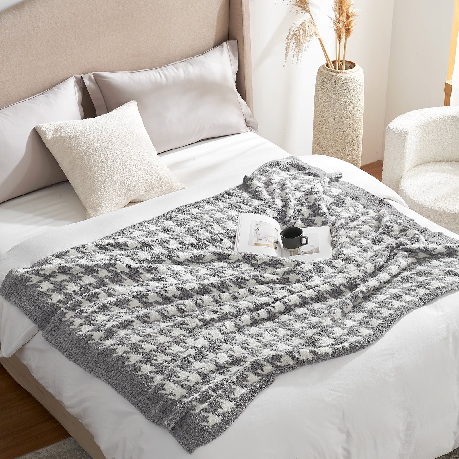 Gray patterned blanket on a bed with pillows and a vase in the background #color_Grey