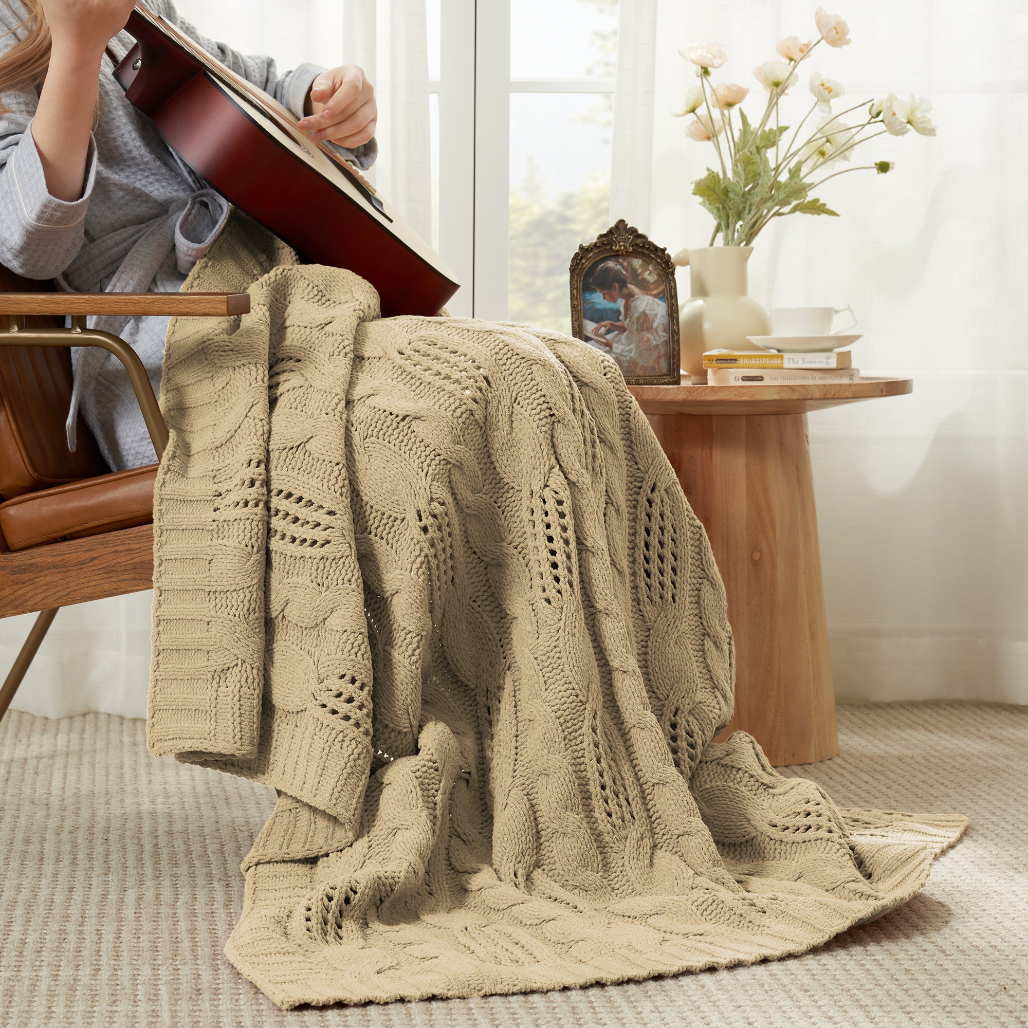 Woman sitting on chair with a Snuggle Sac cable chenille knit throw blanket in Beige while playing guitar #color_Beige