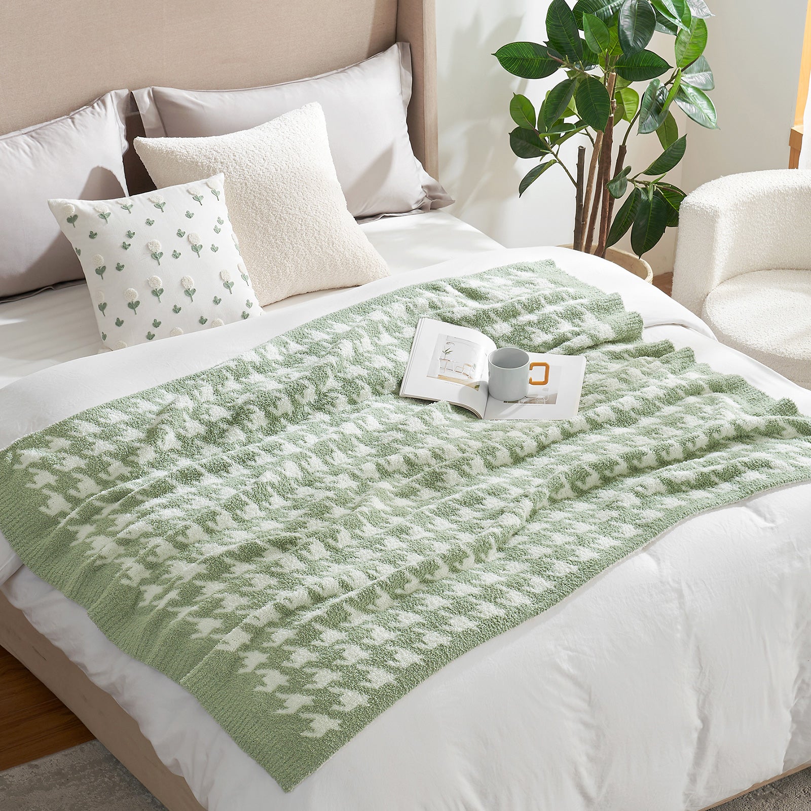 Green knitted blanket on a bed with pillows and a plant in the background #Color_Sage Green