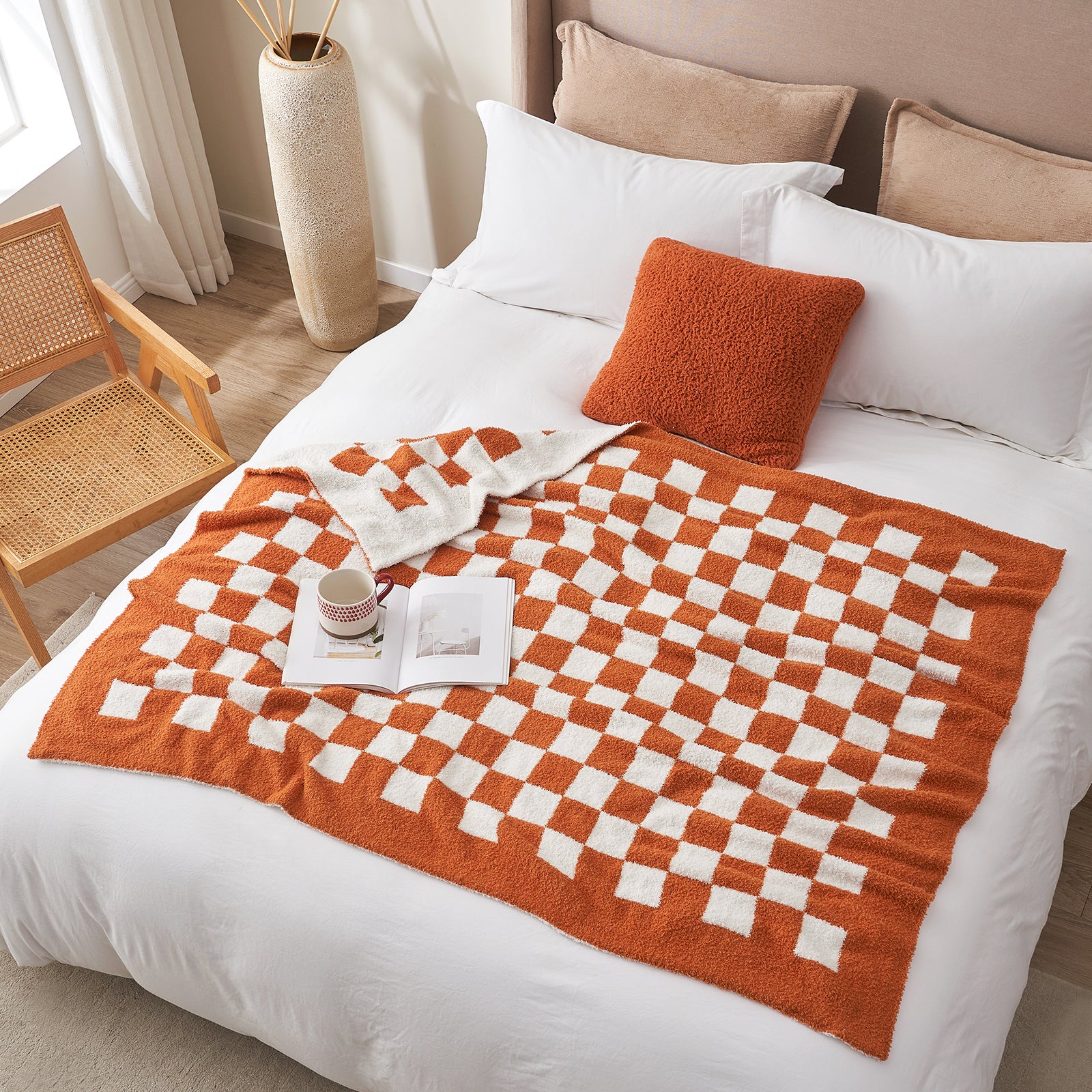 Bed with orange and white checkered blanket, pillows, and a small table with a cup and book. #color_Checkered Burnt Orange