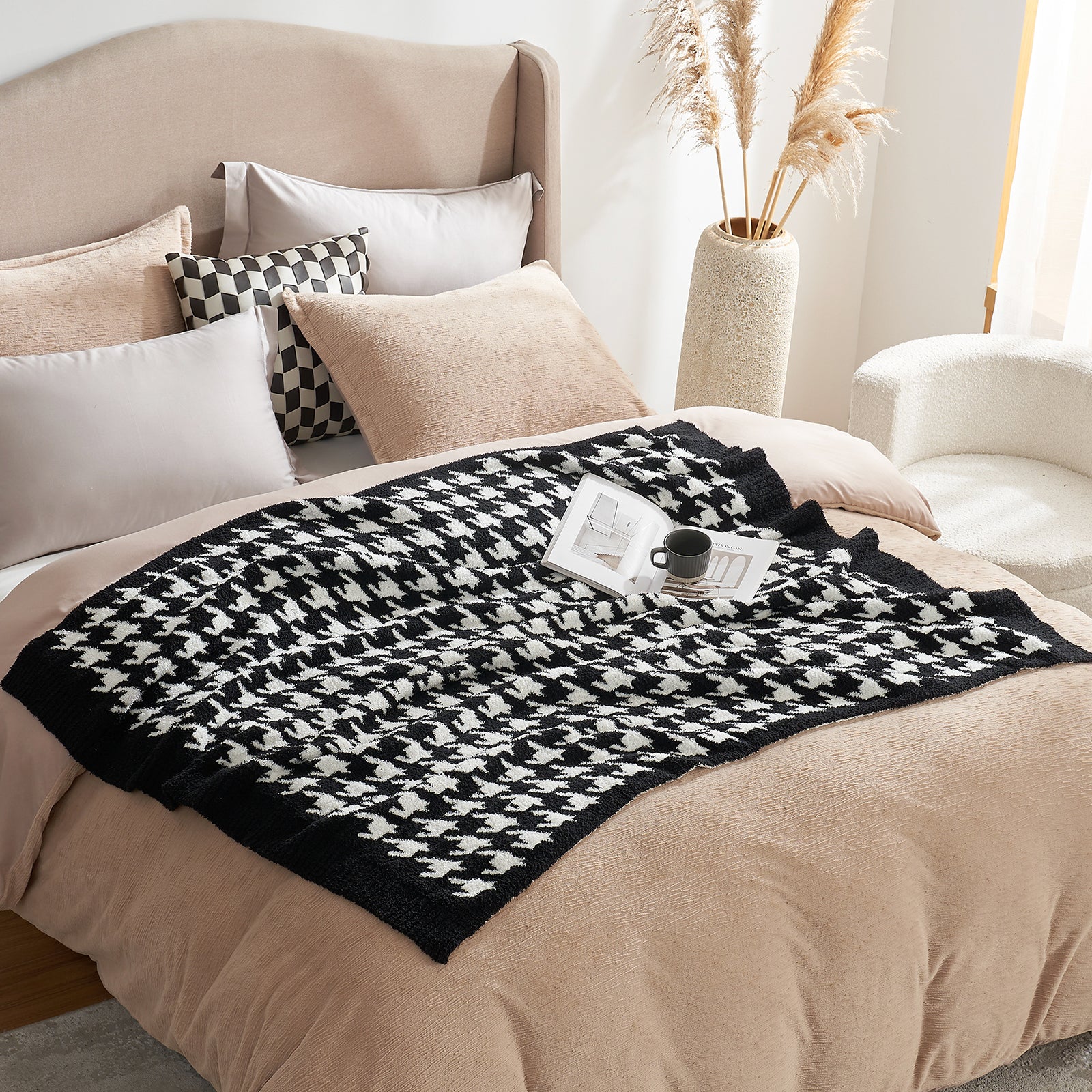 Black and white patterned throw blanket on a bed with pillows and a cup. #color_Black