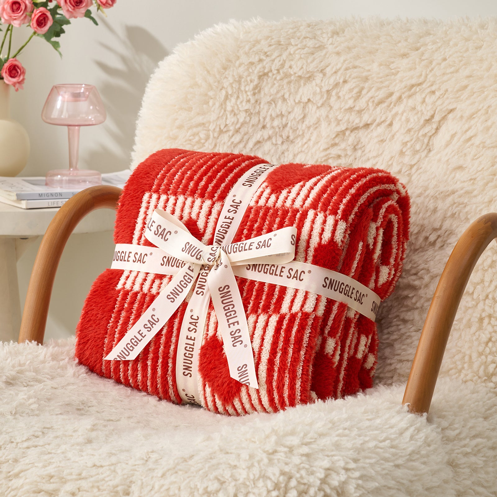 Red and white patterned blanket with 'Snuggle Sac' label on a fluffy chair. #color_Red Heart