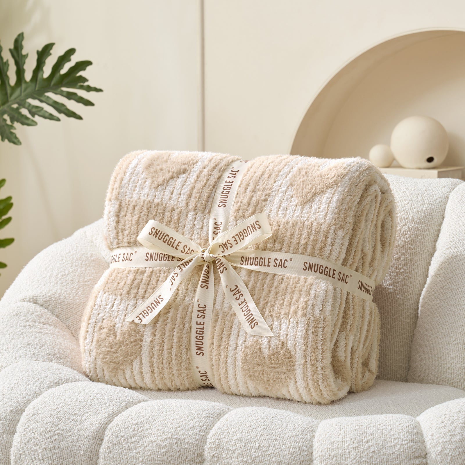 Beige snuggle sac wrapped with a ribbon on a white couch #color_Cream/Beige