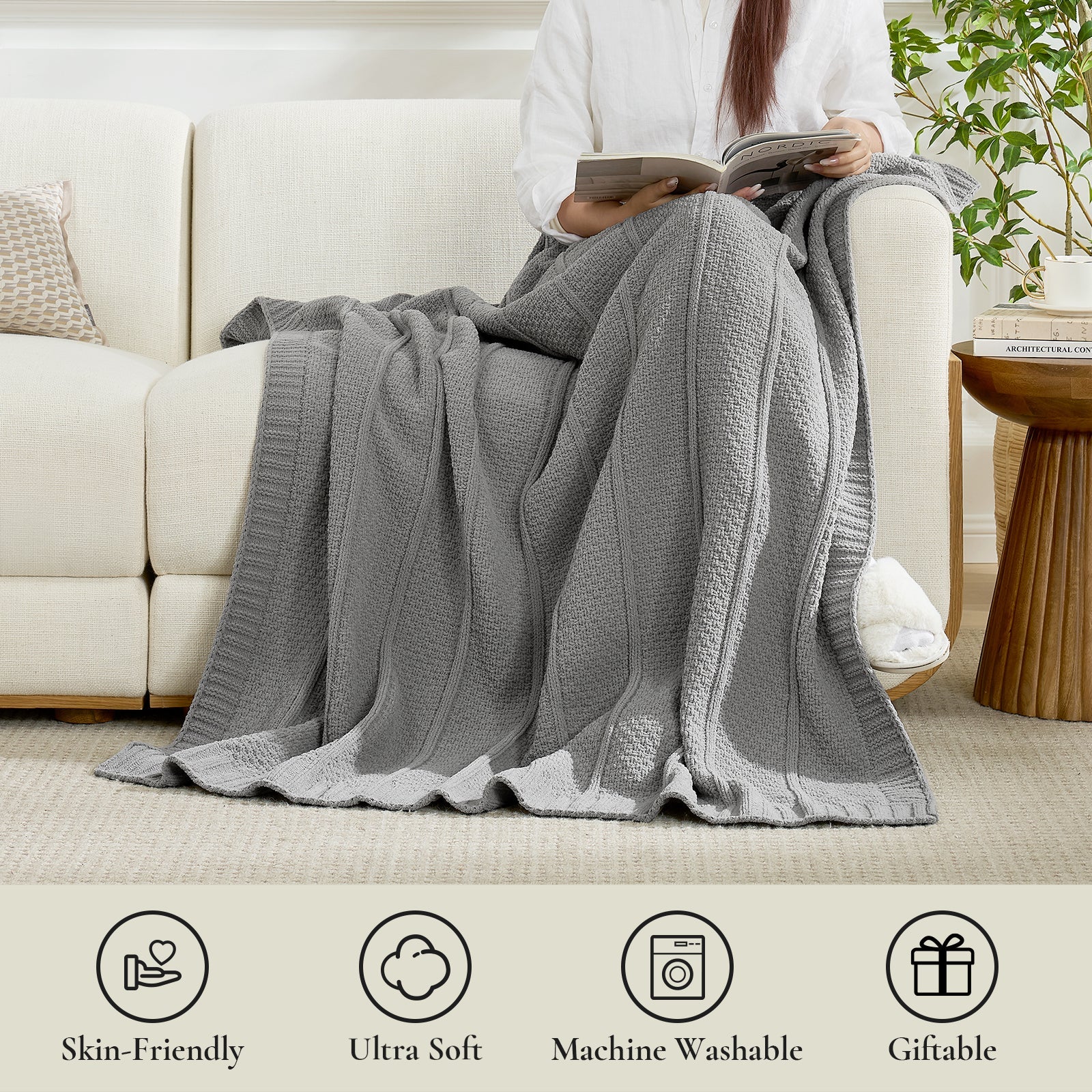Person sitting on a couch with a gray blanket, holding a book, in a cozy living room setting. #color_Gray