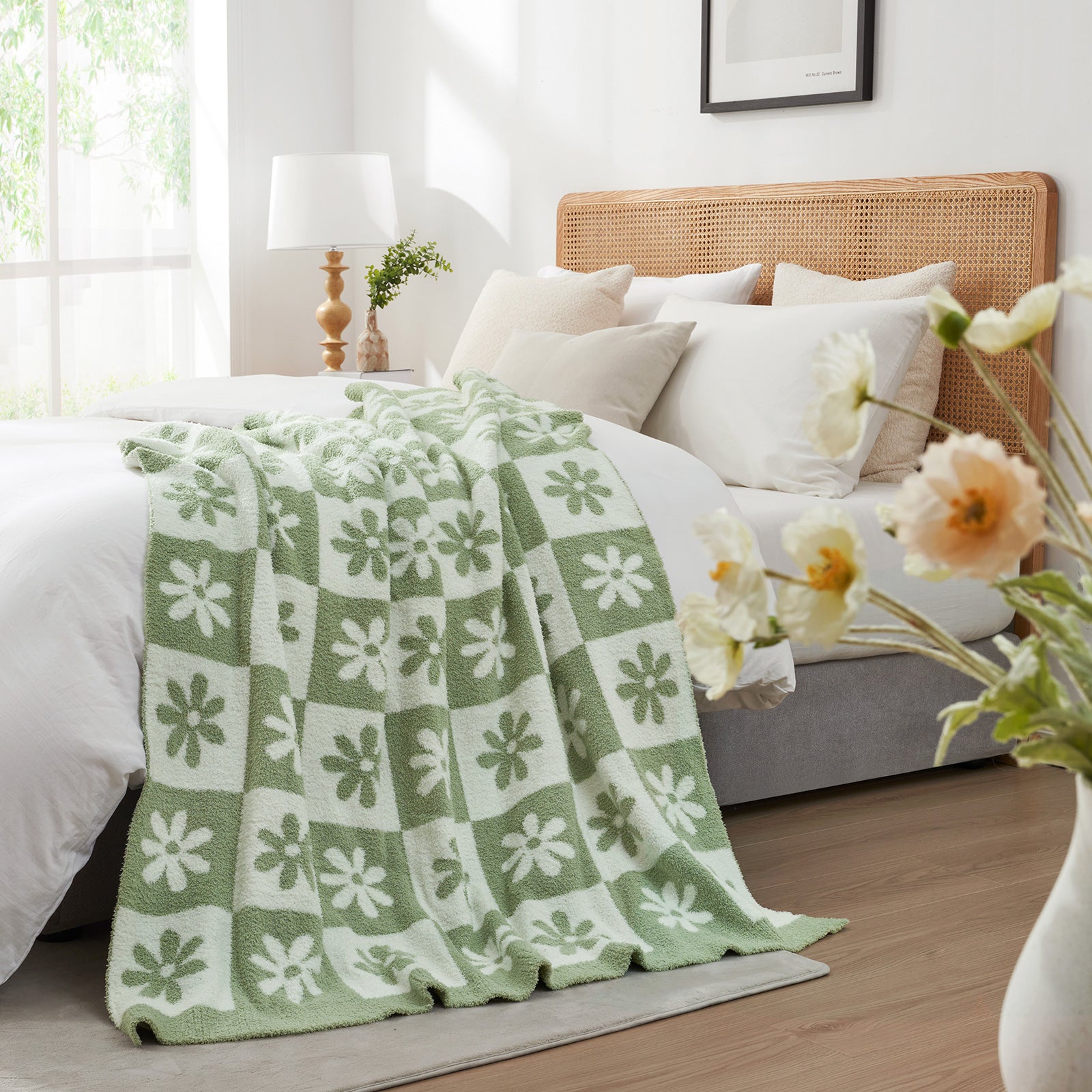 Green and white patterned blanket on a bed in a bright bedroom with flowers and a lamp. #color_Sage Green
