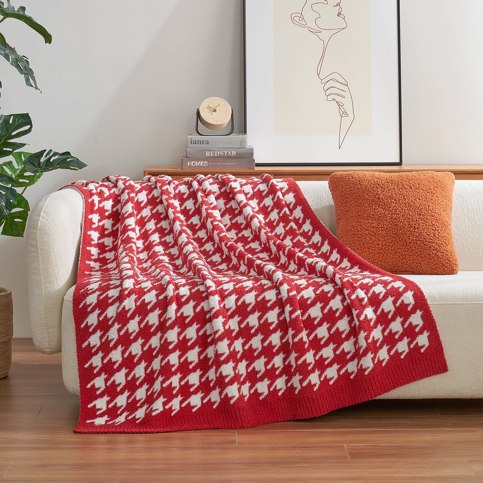 Red and white patterned blanket draped over a white sofa with an orange pillow, in a living room setting. #color_Red
