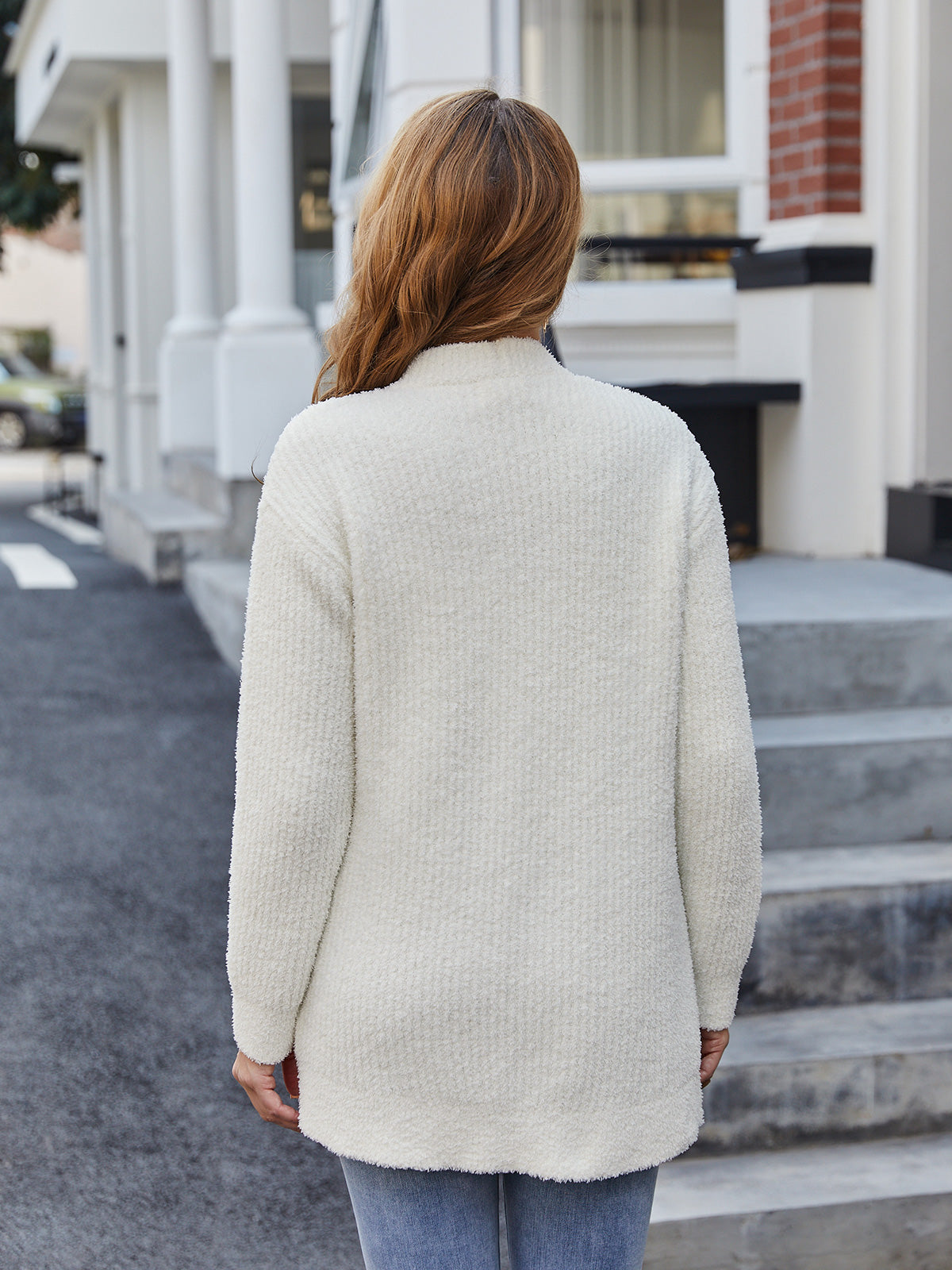 Person wearing a cream-colored cardigan walking on a street. #color_cream