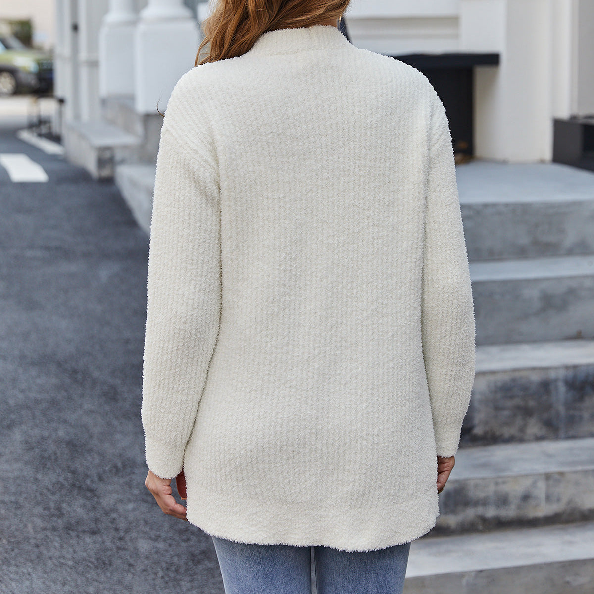 Person wearing a cream-colored cardigan walking on a street. #color_cream