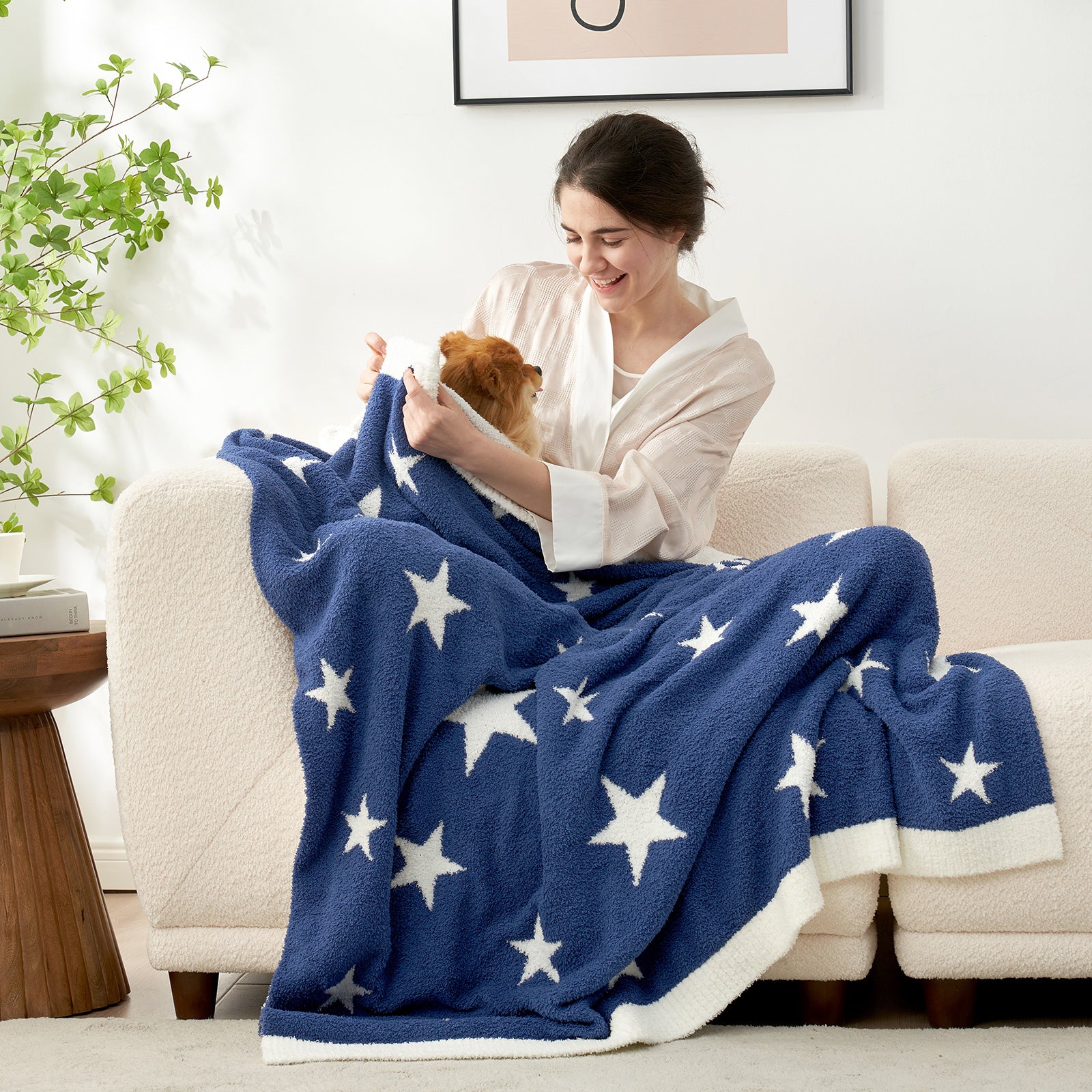 A woman with a dog sitting on a beige couch with Snuggle Sacs Reversible Star Feather Yarn Knit Throw Blanket#color_Royal_Heather_Blue