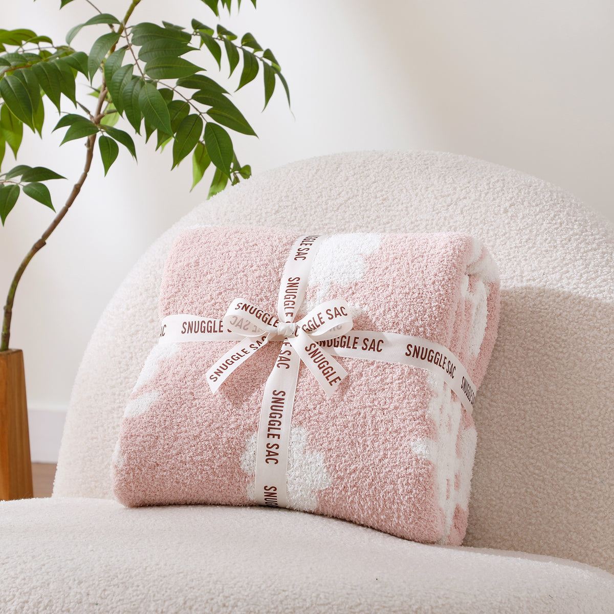 Folded flower blanket with 'Snuggle Sac' branding on a pink surface, accompanied by decorative flower print. #color_Pink