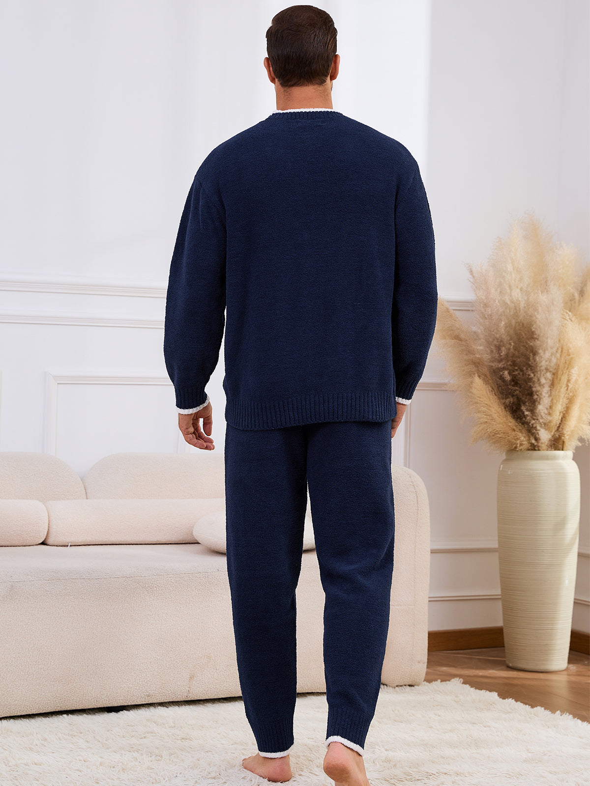 Man wearing navy blue pajamas standing in a living room. #color_Navy