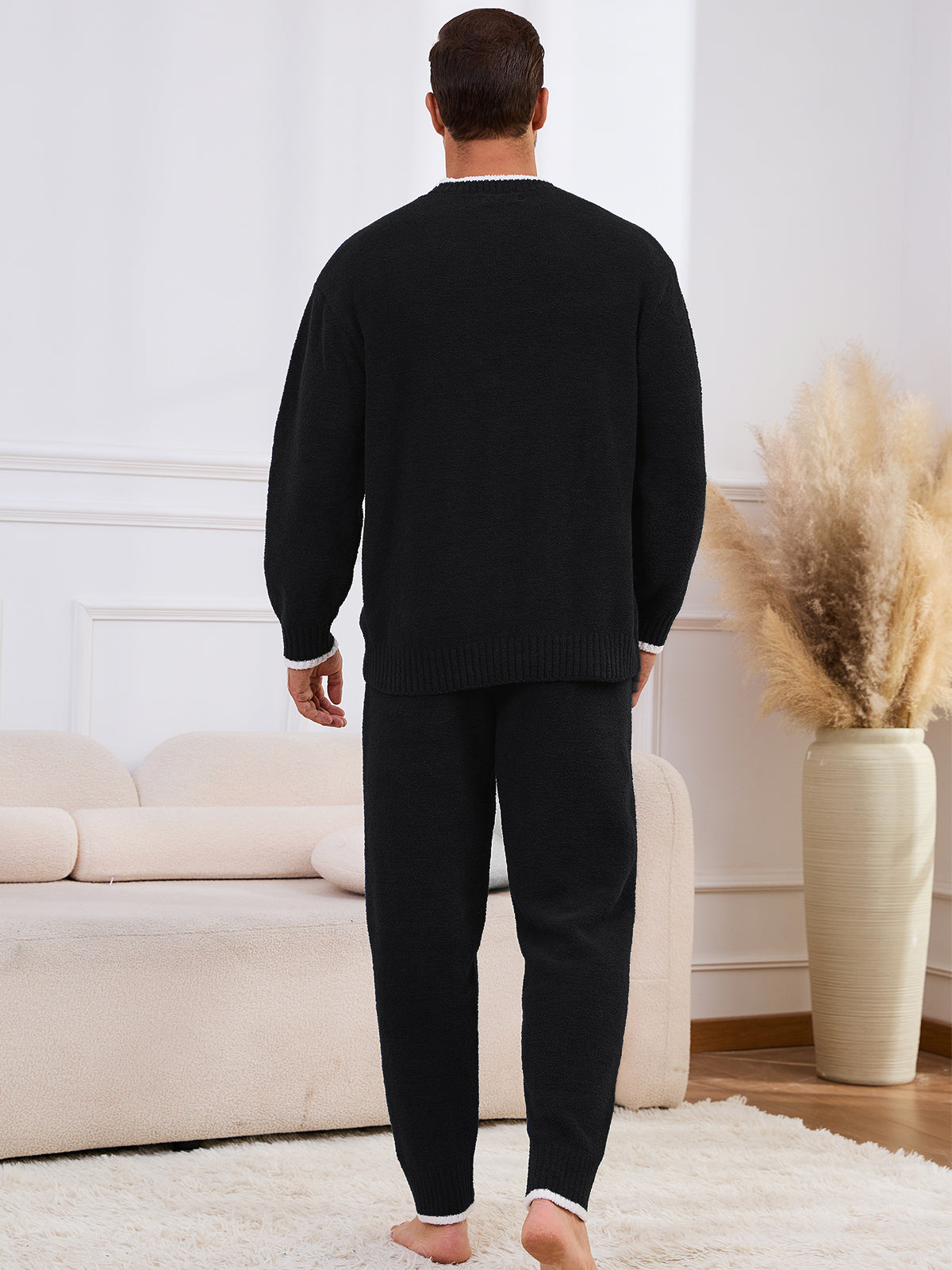 Man wearing a black sweater and pants in a living room setting. #color_Black