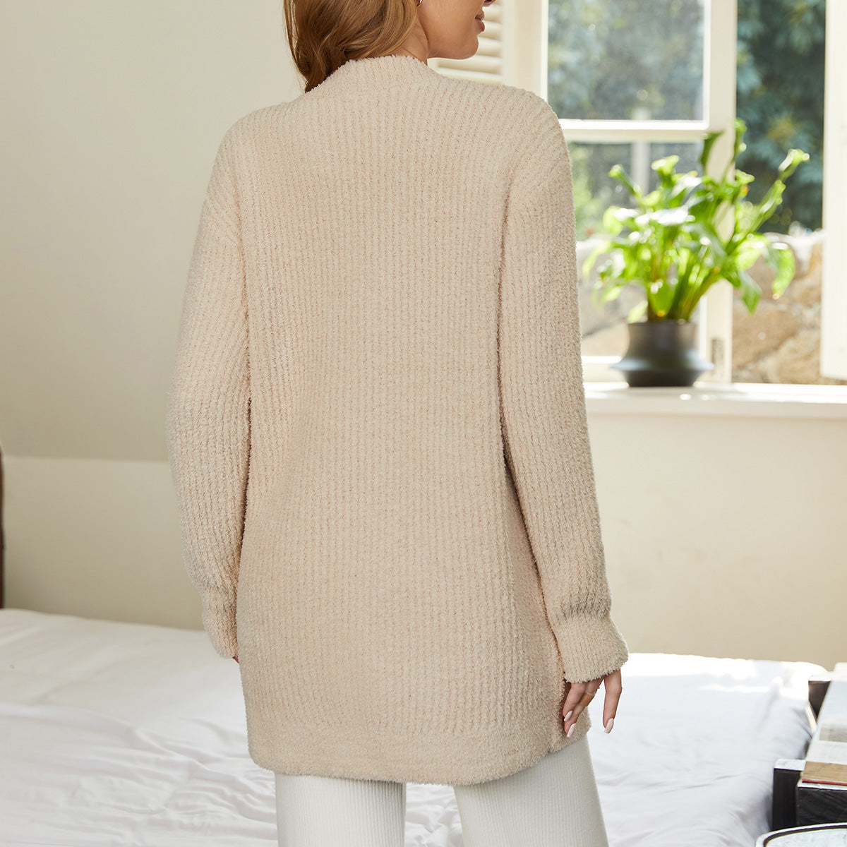 Woman wearing a beige cardigan standing in a room with a window and plants. #color_Beige