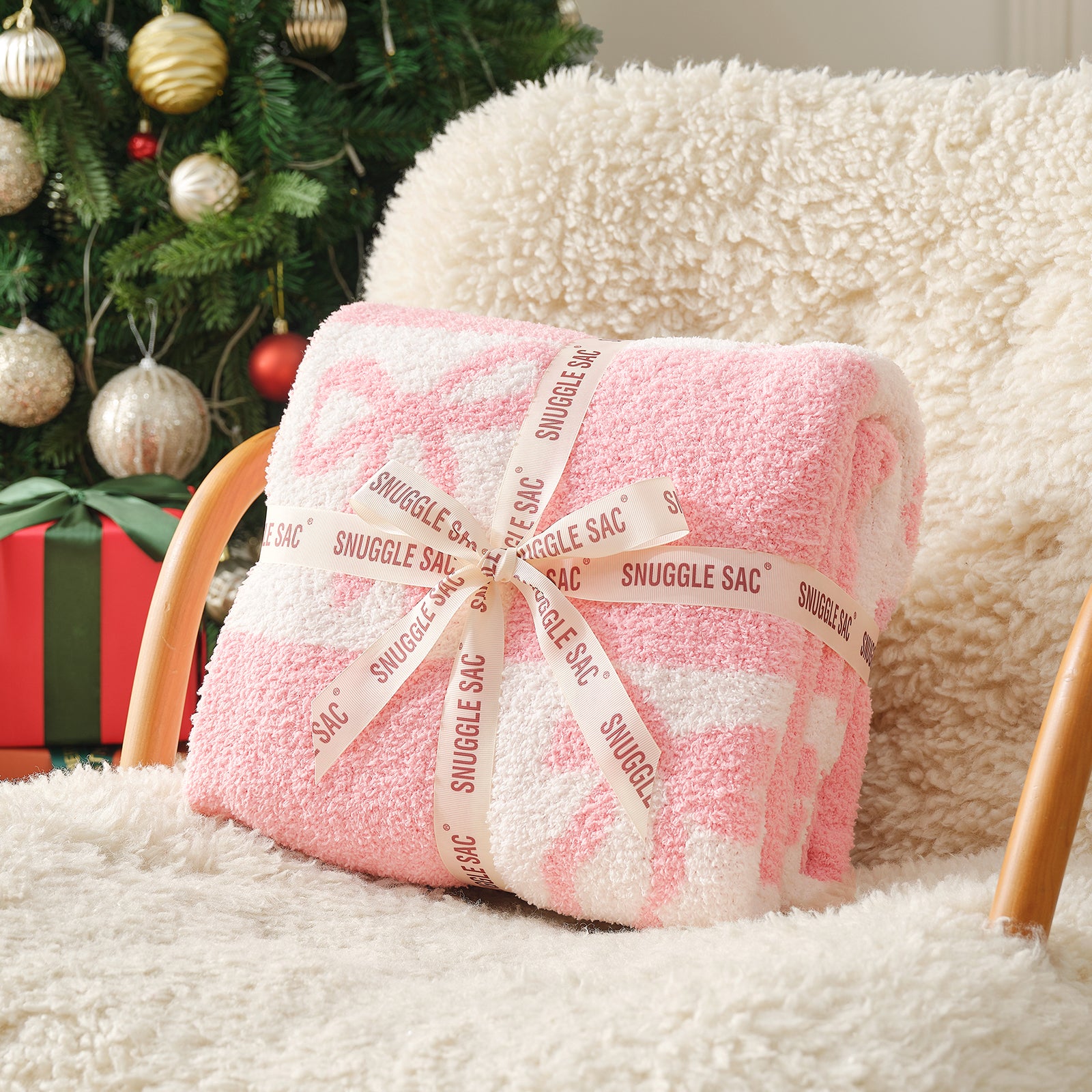 Pink snuggle sac wrapped in ribbon on a white surface with a Christmas tree in the background #color_Pink Bow