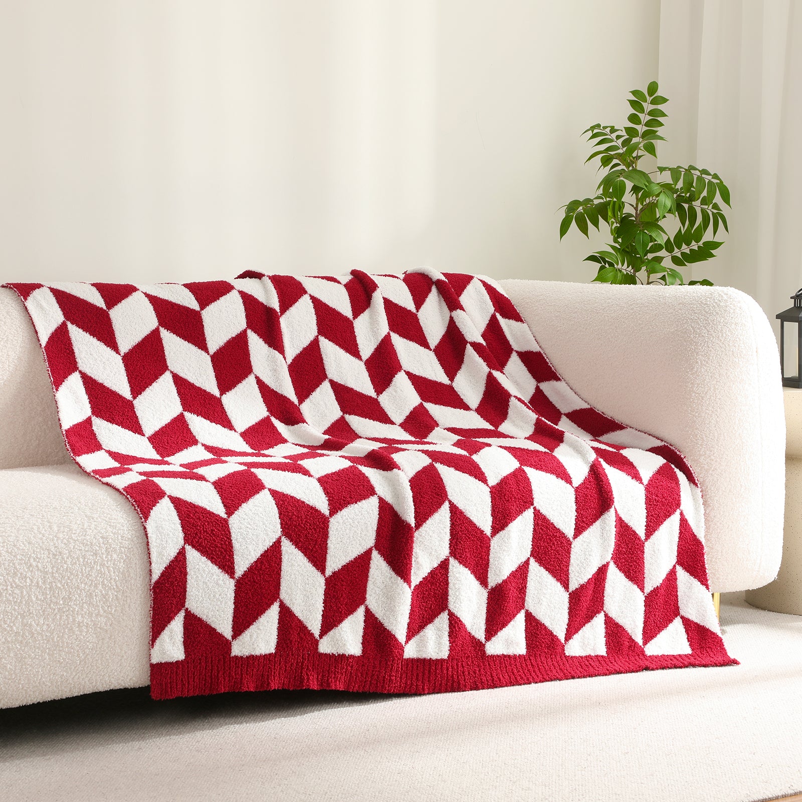 Red and white geometric patterned blanket on a beige sofa with a plant in the background #color_Red