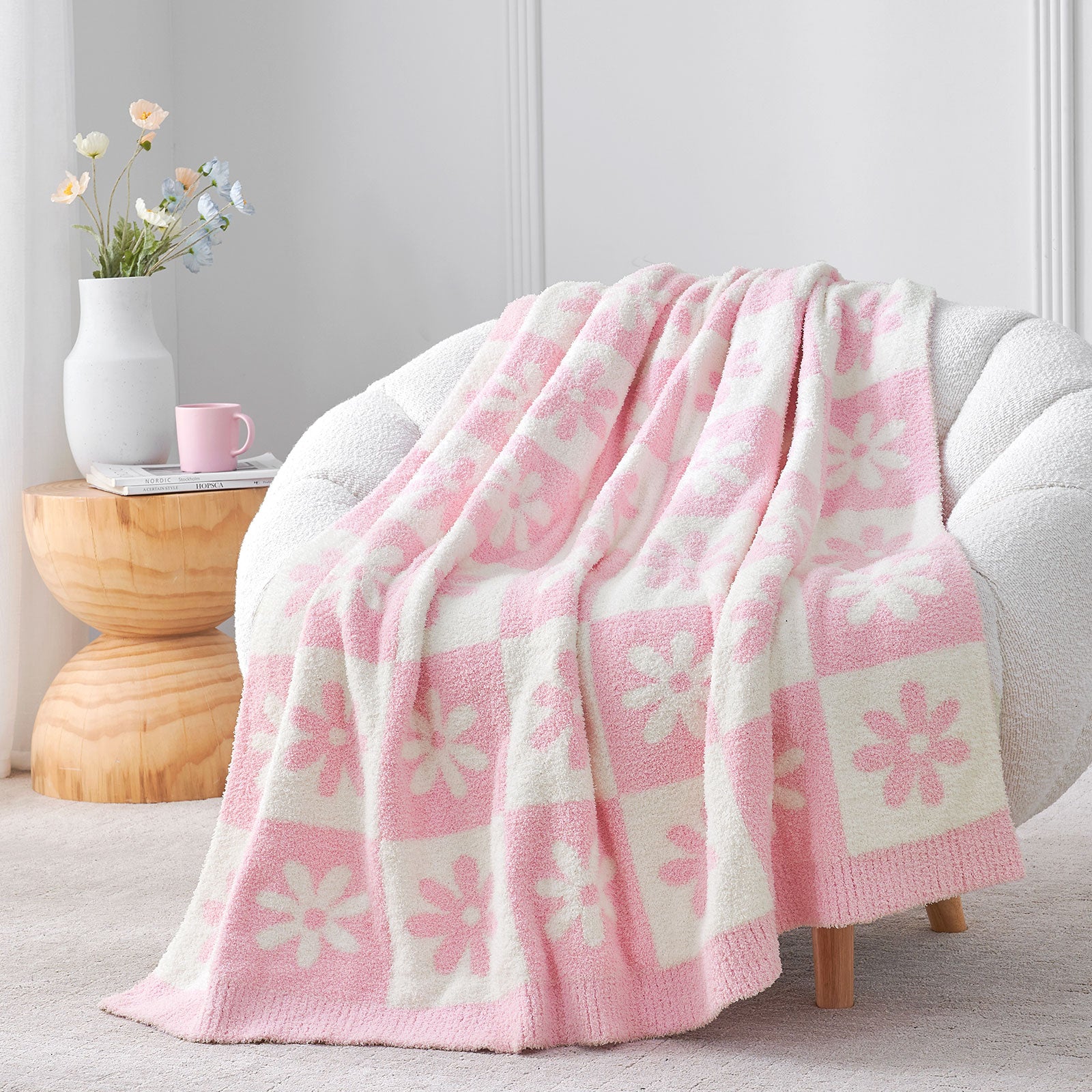 Pink and white floral-patterned blanket draped over a chair in a cozy room. #color_Baby Pink