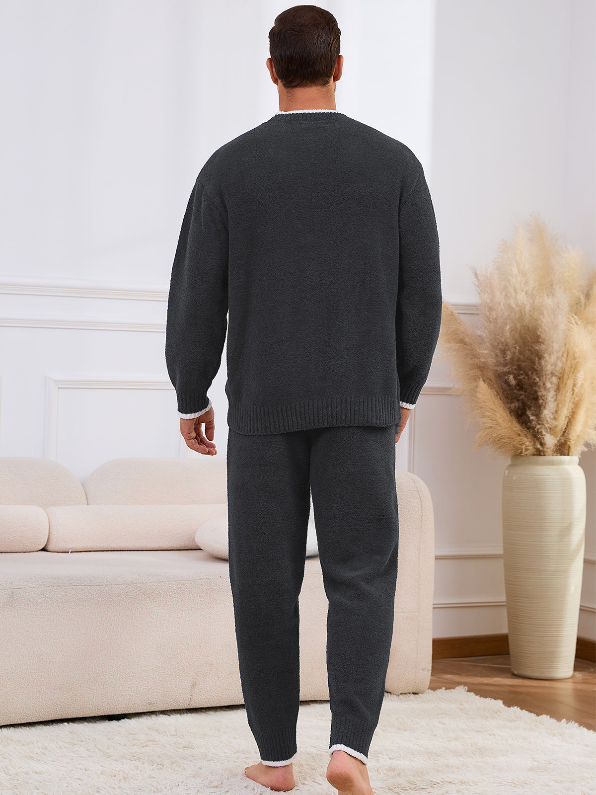 Man wearing a dark gray sweater and pants in a living room setting. #color_Dark Grey