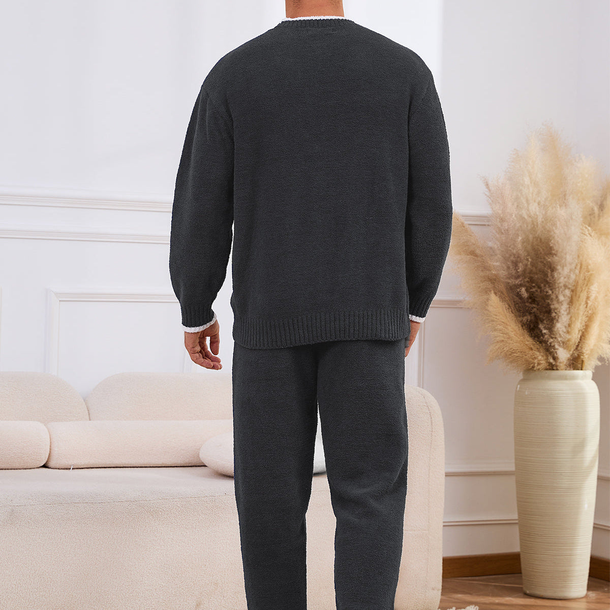 Man wearing a dark gray sweater and pants in a living room setting. #color_Dark Grey