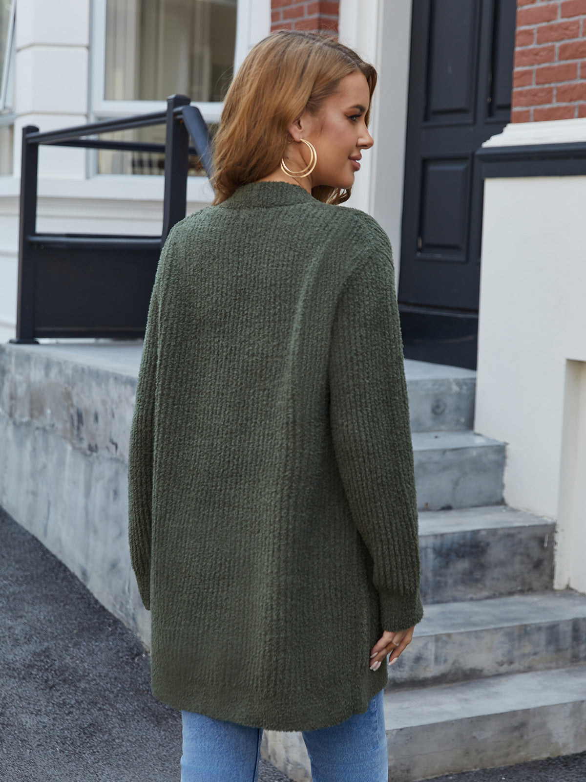 Woman wearing a green cardigan standing on steps outside a building. #color_Army Green